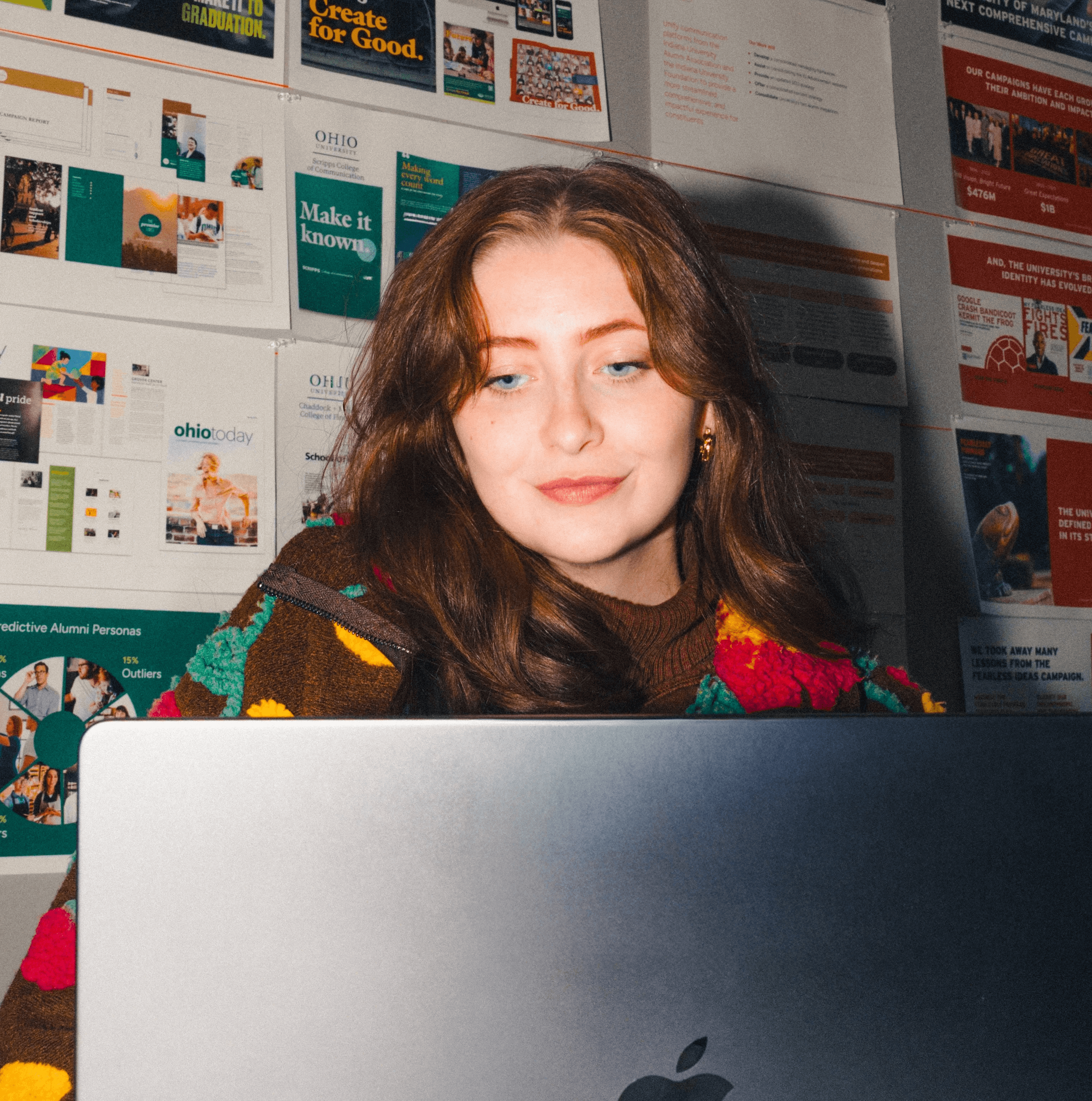 A thoughtful young person with long brown hair looks down at computer, flash photography style