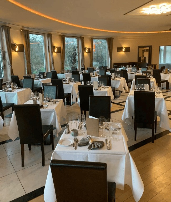 Restaurantbereich eingedeckt mit weißen Tischdecken und Geschirr