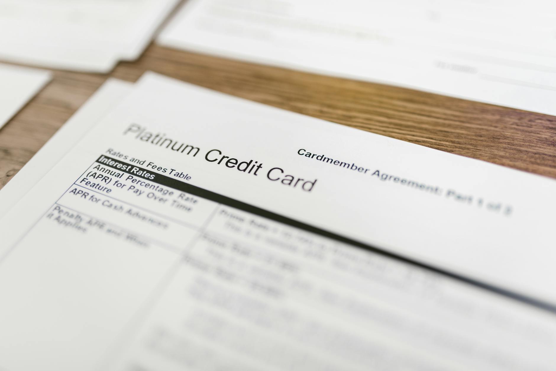 Close-up of a platinum credit card cardmember agreement document showing interest rate tables on a wooden surface