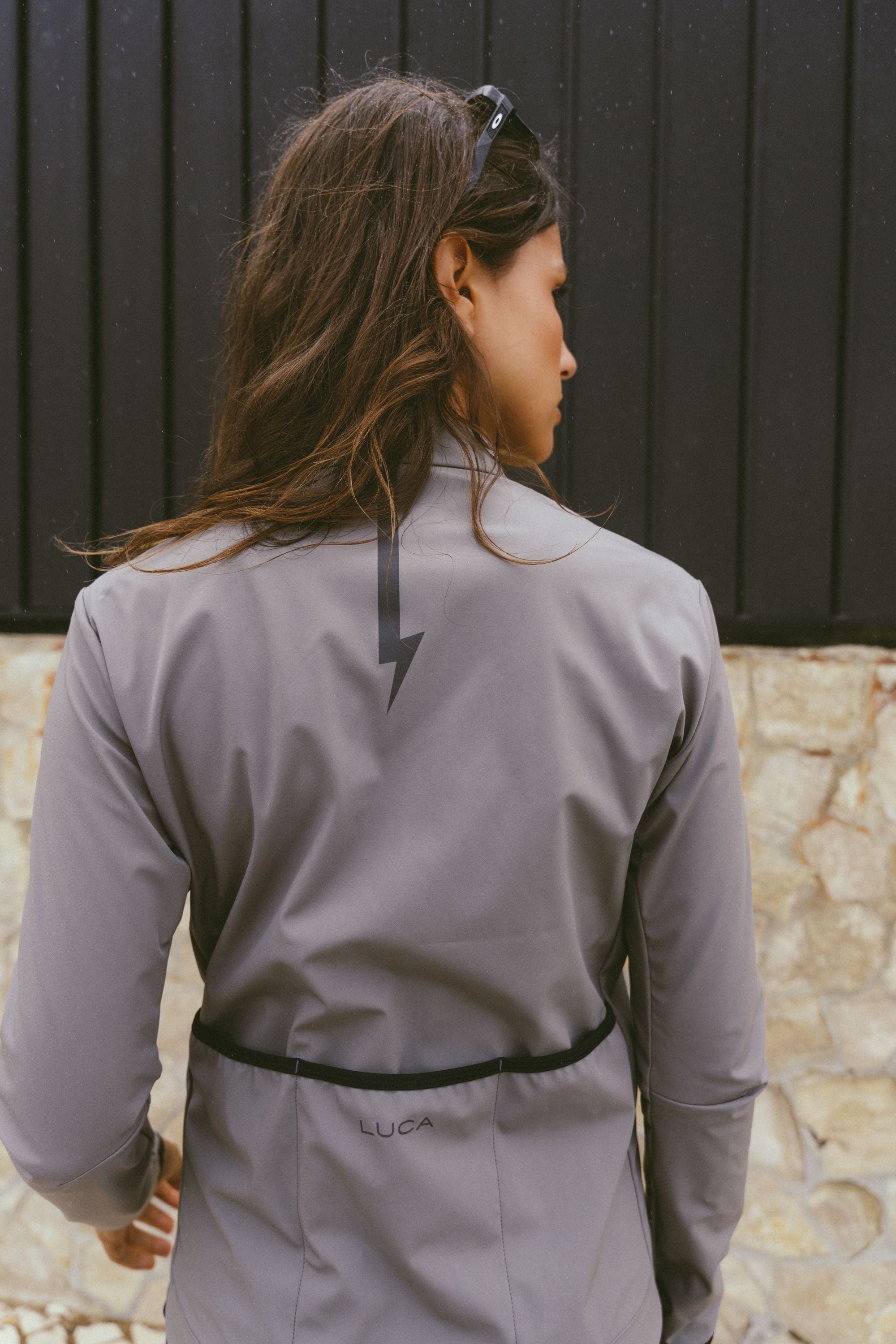 Back-view-of-a-woman-wearing-the-Momentum-jacket-in-Grey-with-large-black-lighting-bolt-sign-and-LUCA-text