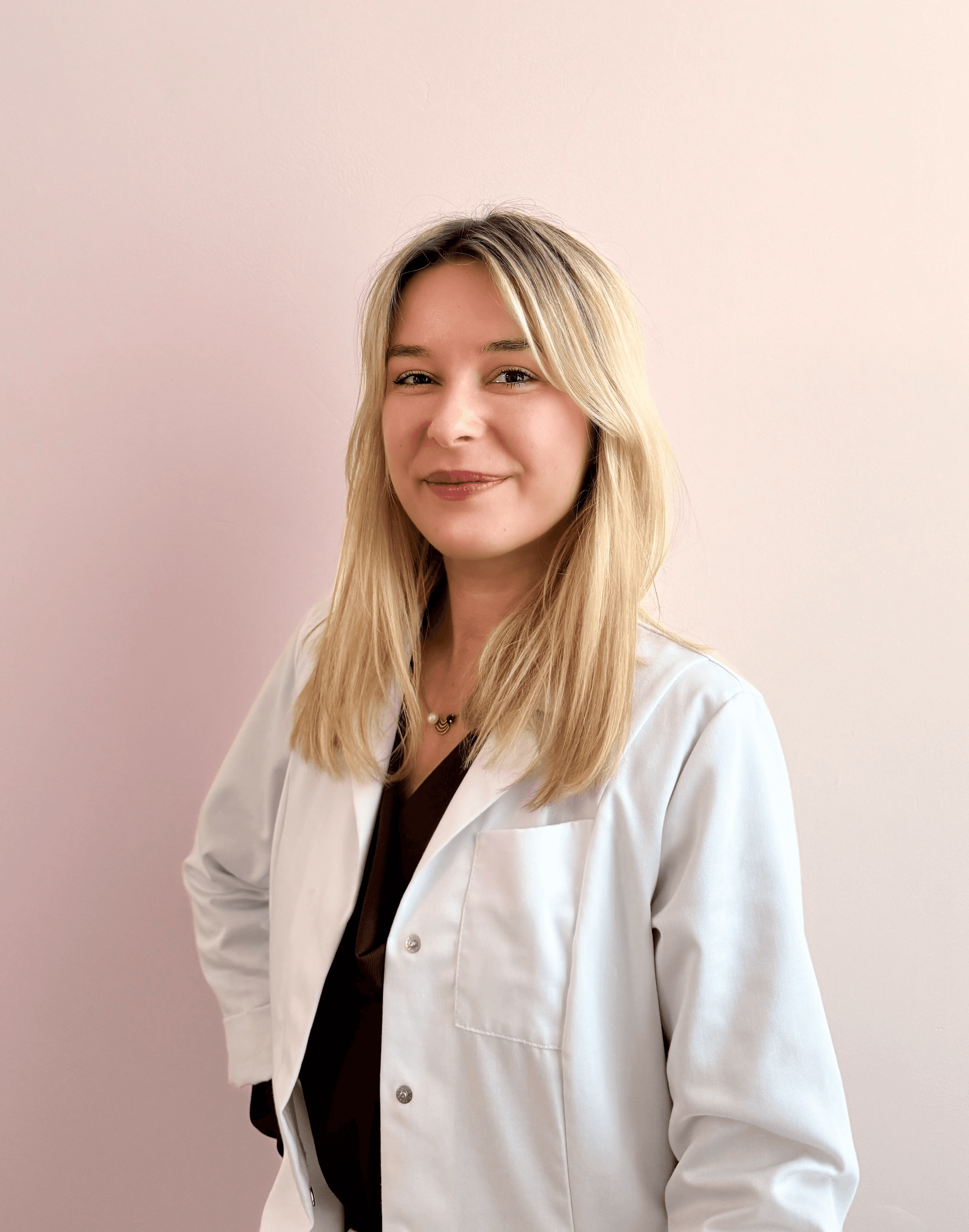 Portrait of Dr. Louise Cuveele, aesthetic doctor and founder of Cuveele's Clinic, wearing a white coat and smiling at the camera.