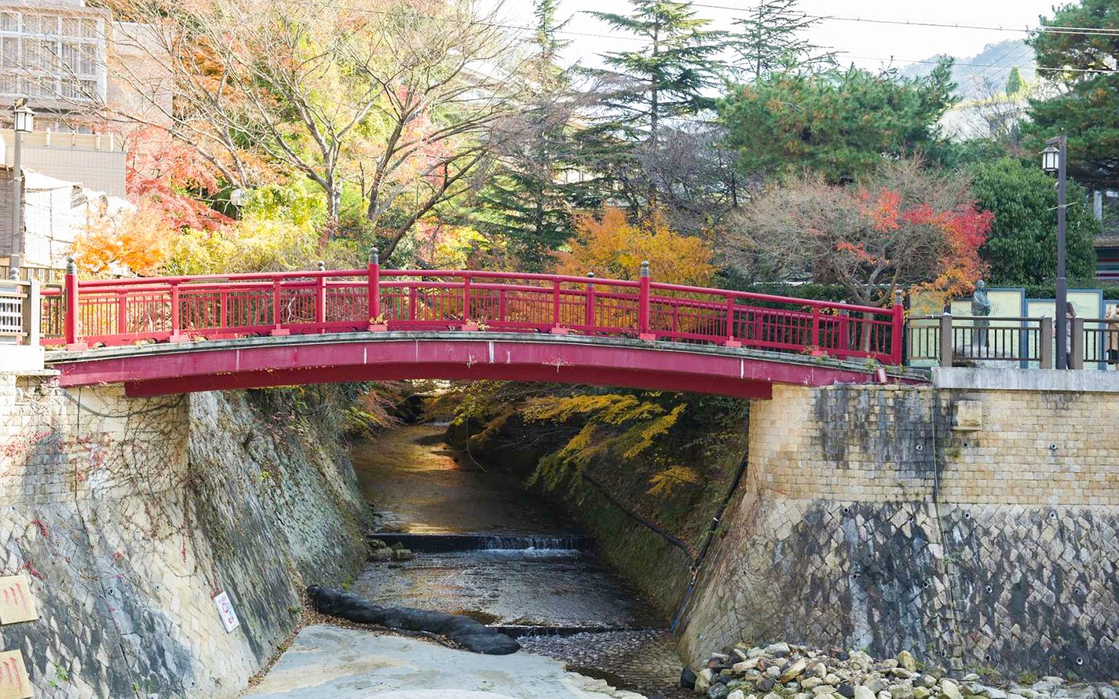 Red bridge over a stream surrounded by autumn trees in Arima Onsen, Japan.