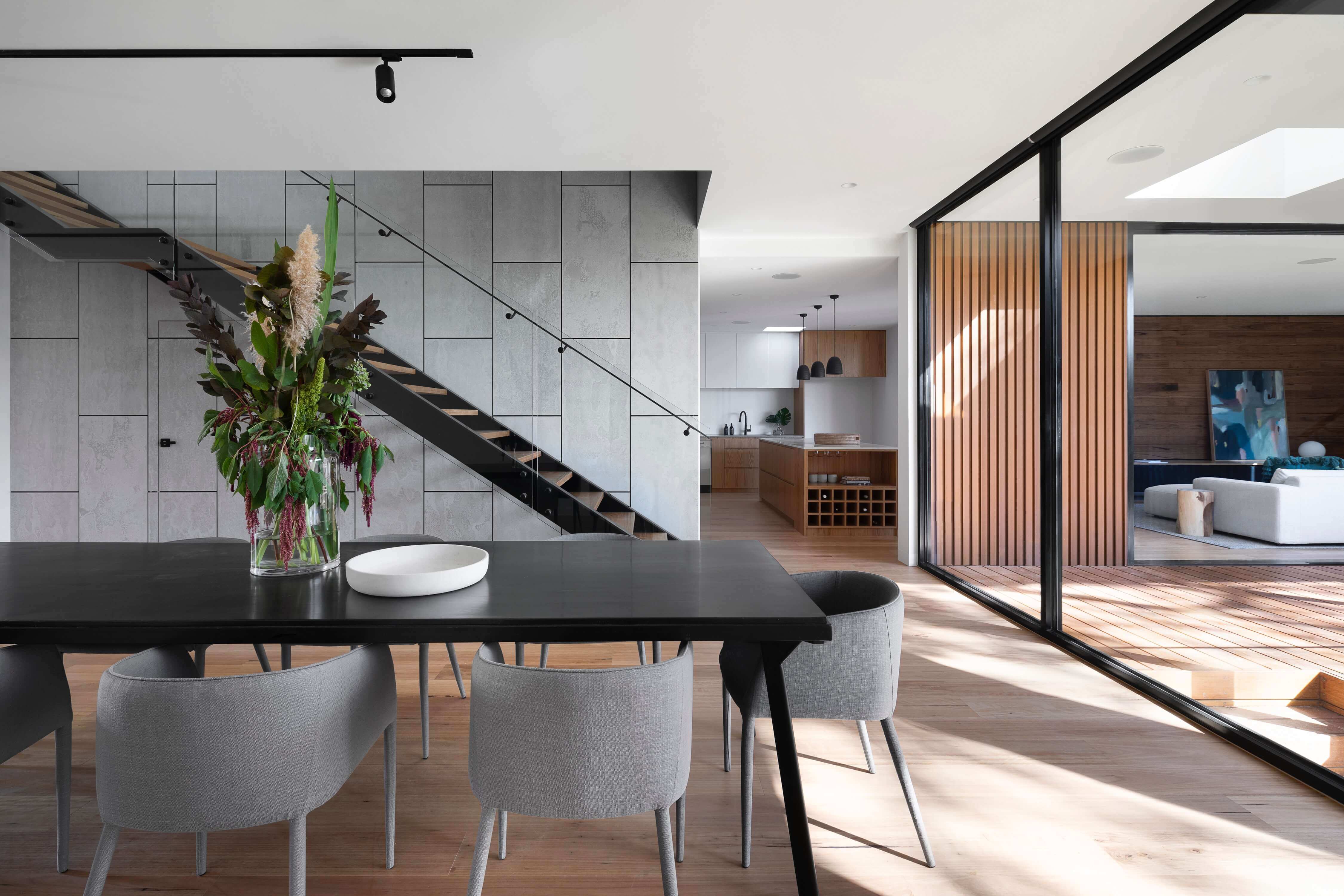 Modern open-plan dining area with a concrete feature wall and timber staircase