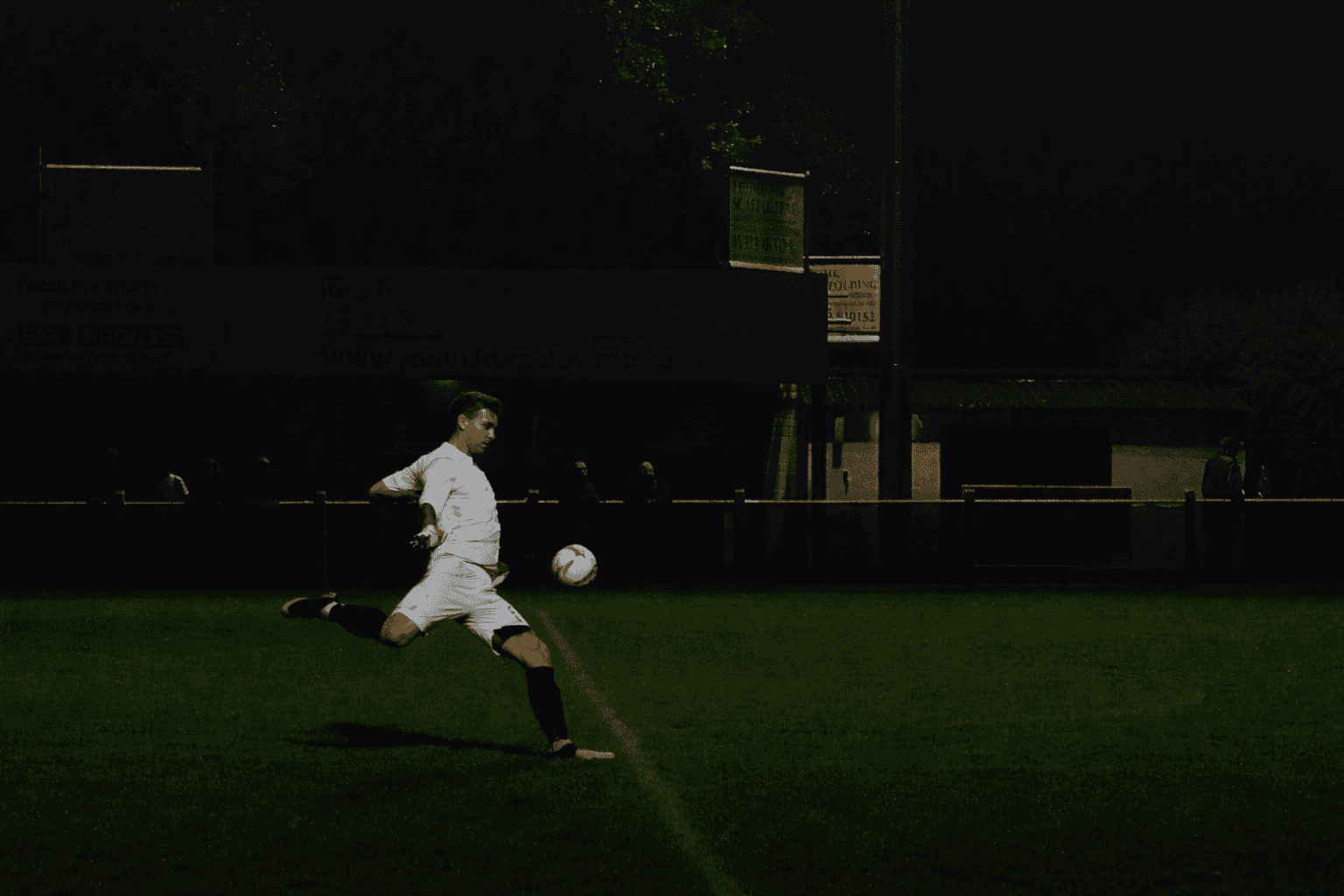 Piłkarz uderzający w piłkę na ciemnym boisku