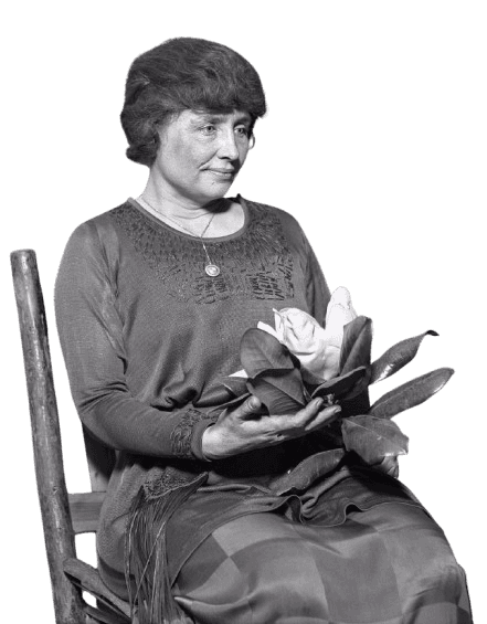 Black and white portrait of Helen Keller, the renowned author, educator, and advocate for people with disabilities. She is seated, holding a magnolia flower, wearing a detailed dress with a pendant necklace. Keller's calm expression and poised posture capture her strength and dignity, symbolizing her role as an influential figure in overcoming adversity.