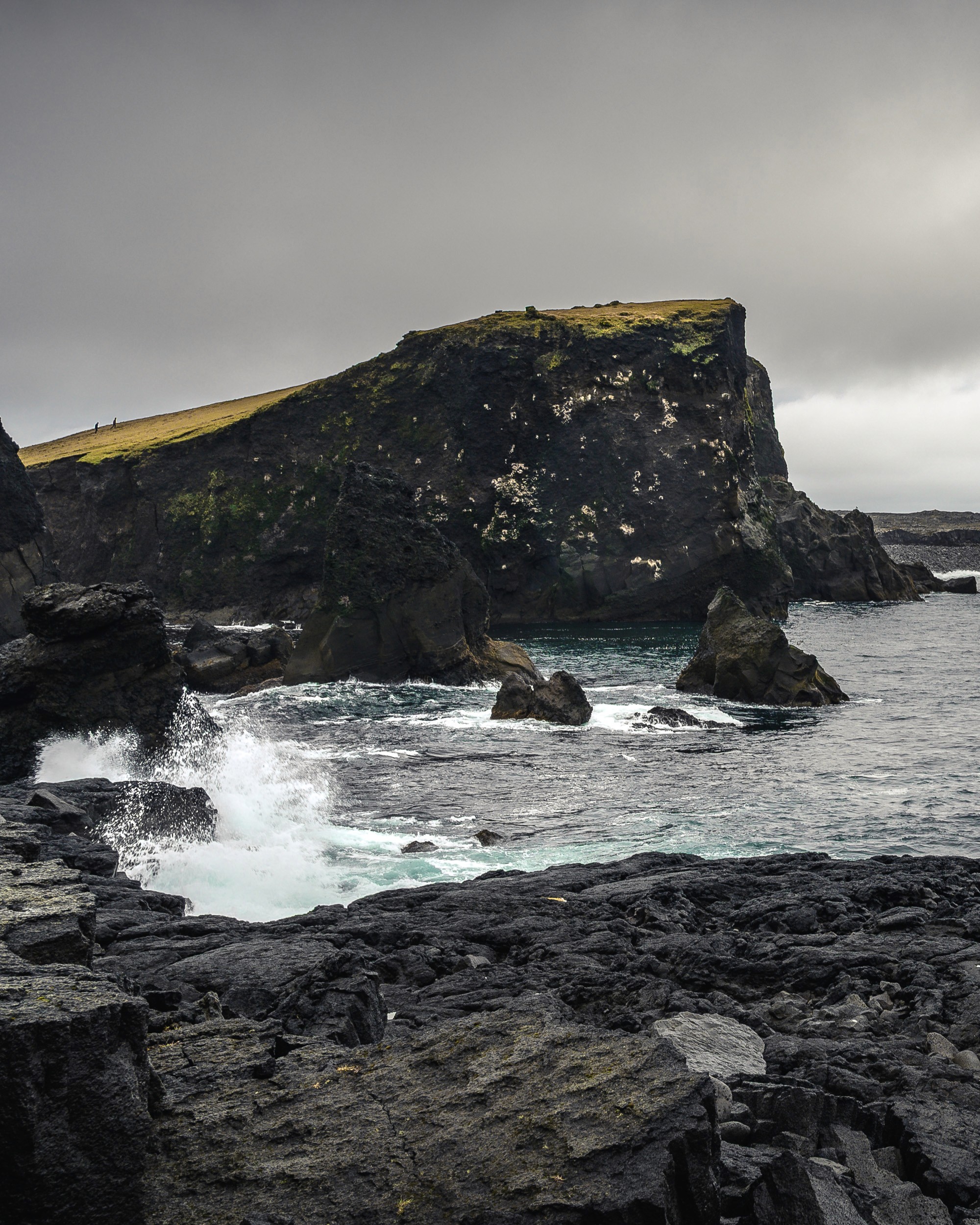 Reykjanes Peninsula with waves crashing and an outlet with people walking up. Iceland