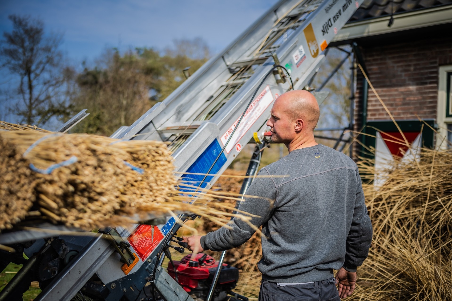Rietdekker van Rietdekkersbedrijf van Dijk werkend aan de vervanging van dakpannen met een rieten dak