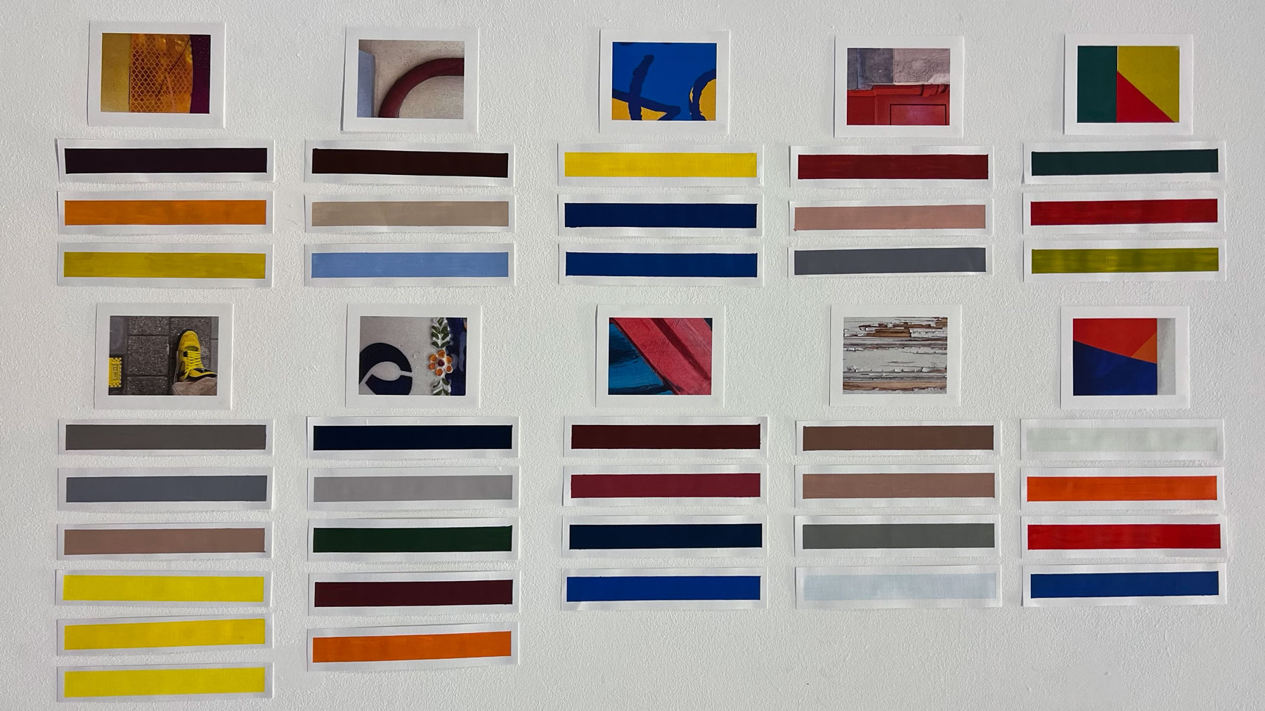 Een geordende presentatie op een witte muur. Bovenaan hangen tien verschillende referentiefoto's. Onder elke foto hangen drie tot vijf horizontale kleurstalen die de dominante kleuren uit de betreffende foto weergeven.
