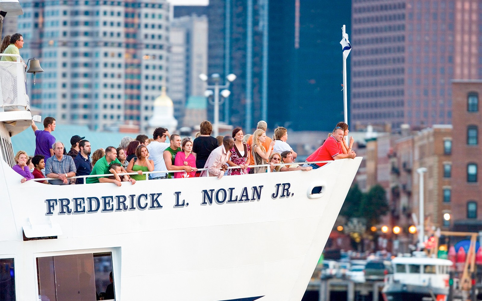 People on a cruise ship in Boston, enjoying city skyline views.