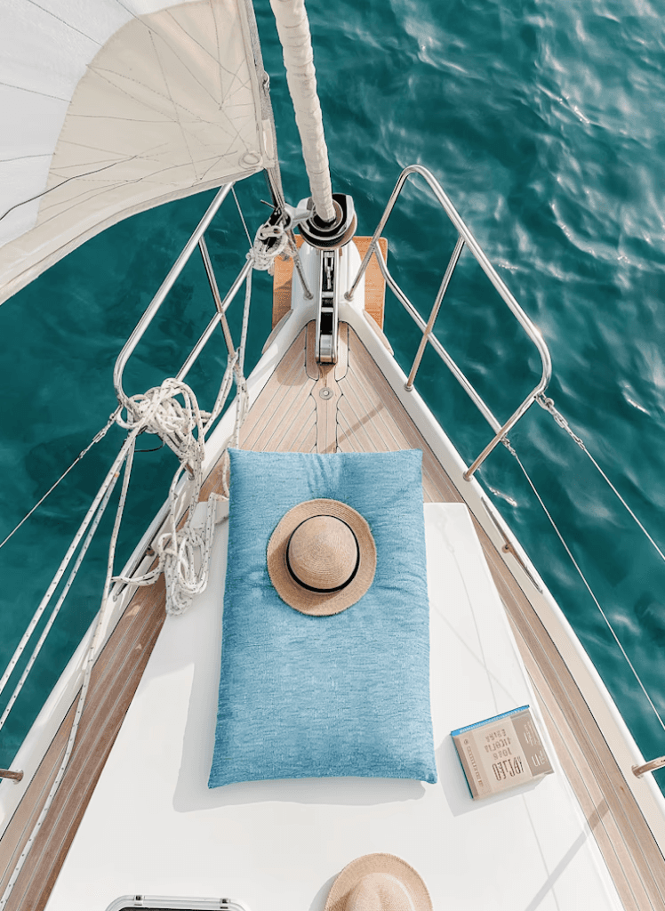 Woman in sun hat and white outfit sitting by poolside with clear water
