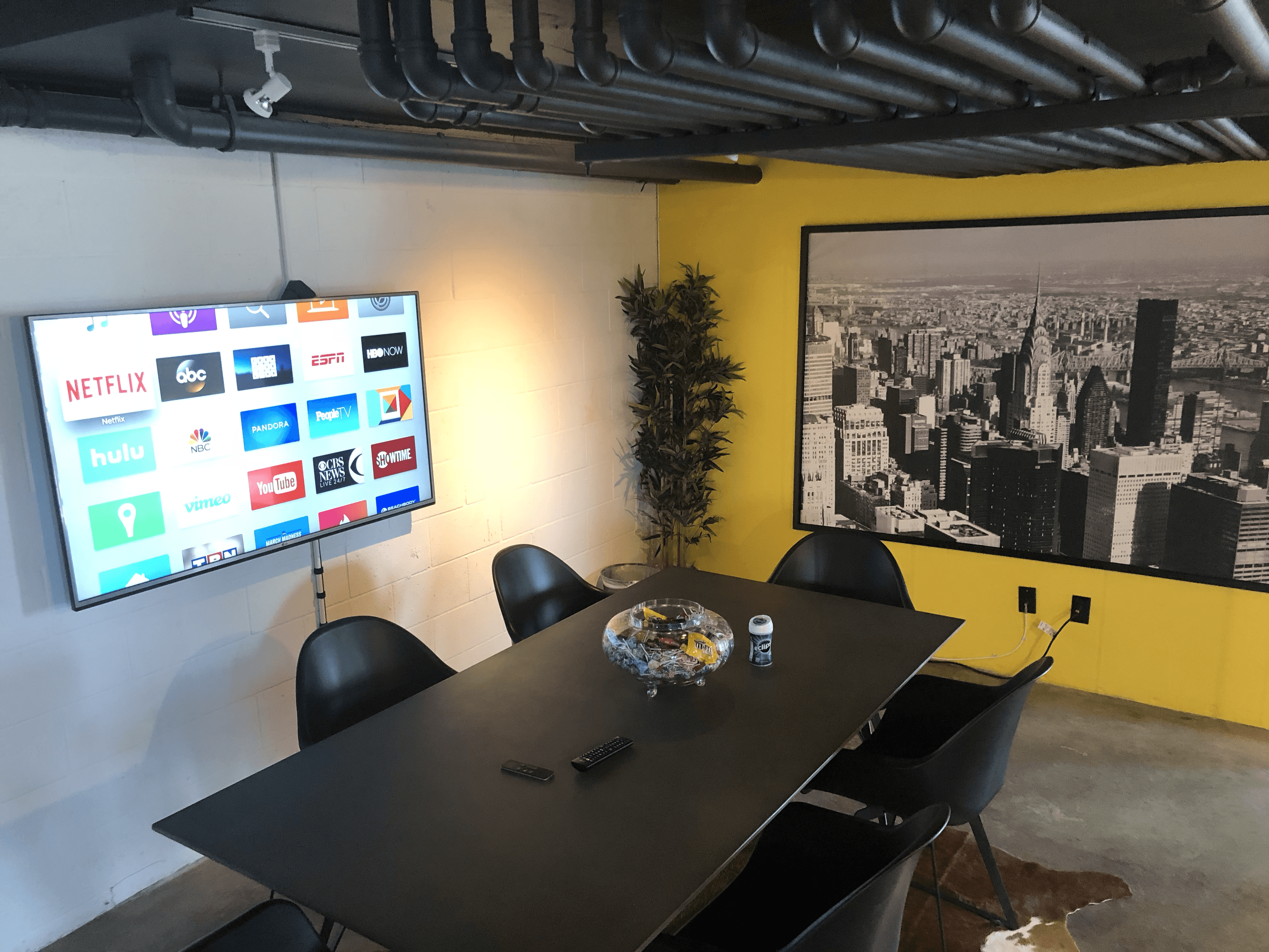 Conference room featuring a large table, black chairs, a TV screen, and a cityscape mural on the wall.