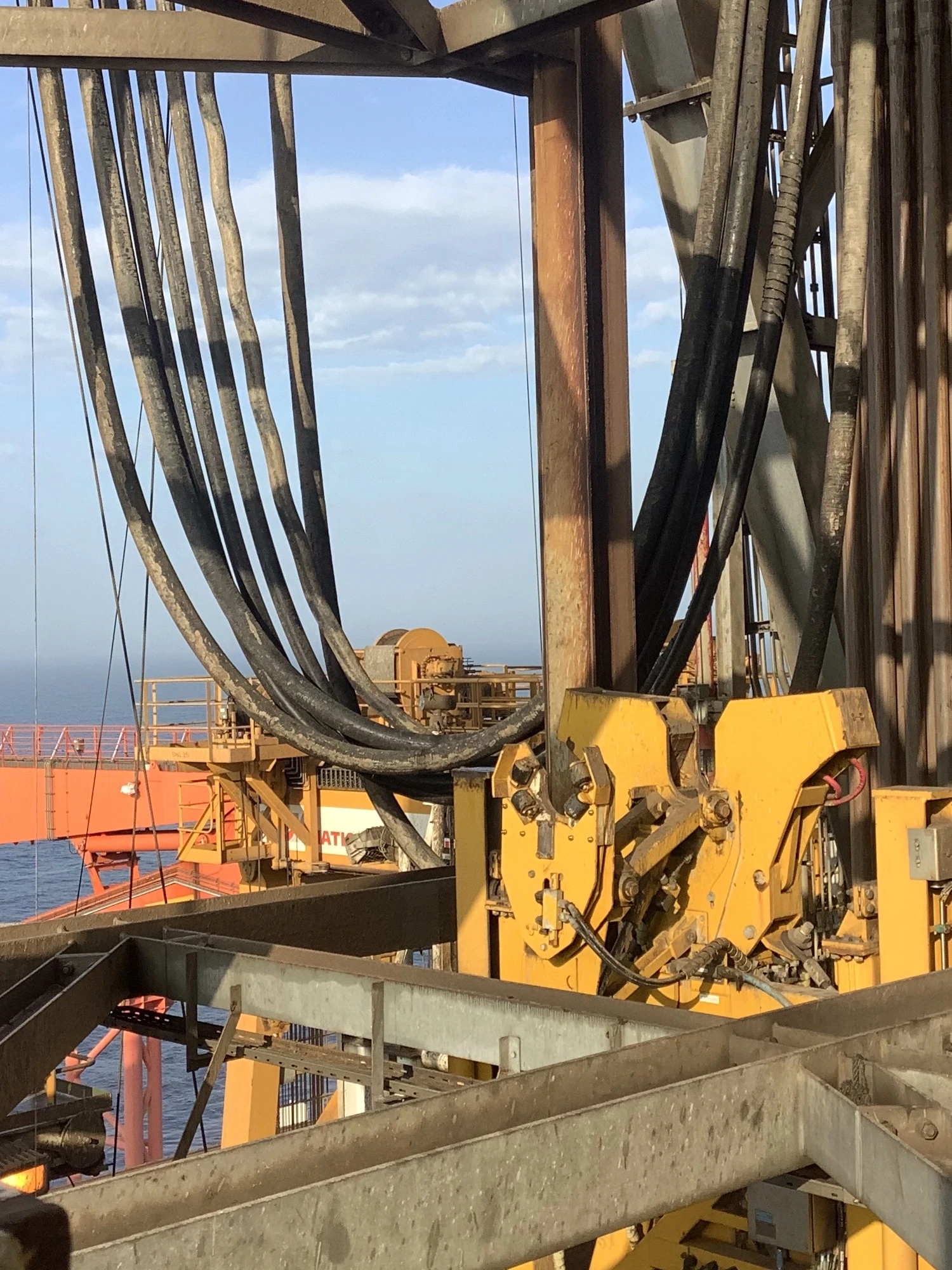 A heavy-duty yellow hydraulic casing tong gripping a steel pipe section on a drilling rig floor.