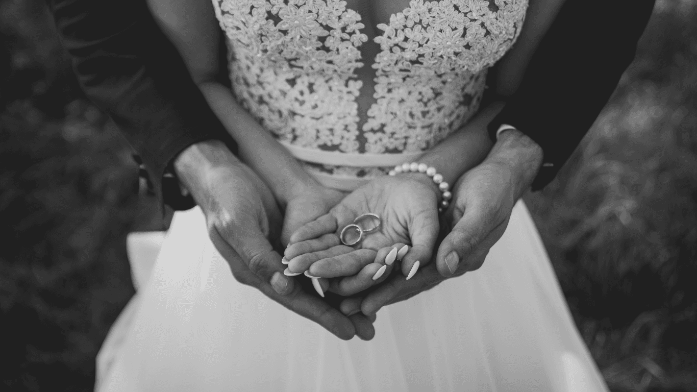 A close-up of hands gently cradling a small baby, set against a soft, natural background in black and white.