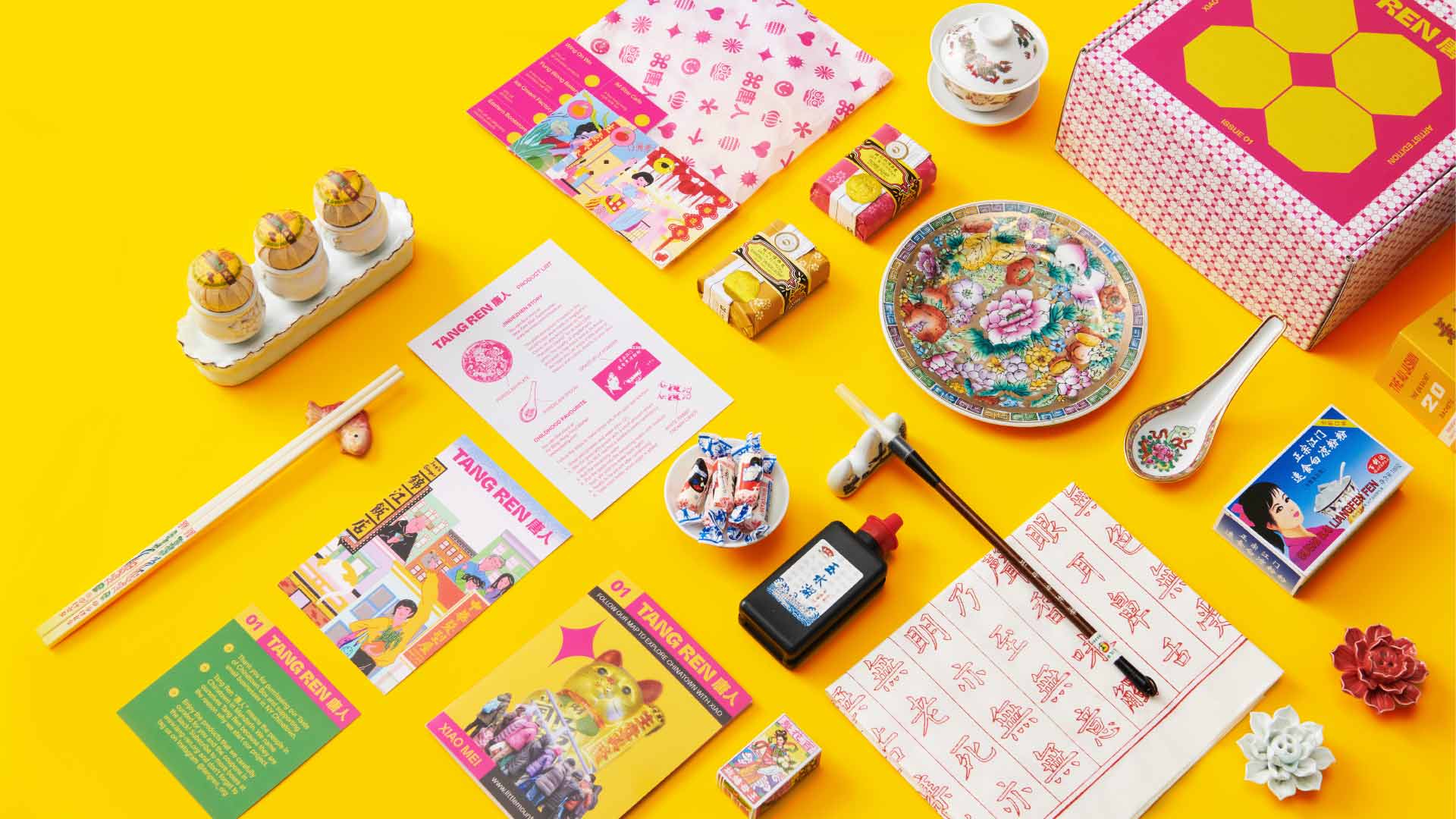 The image shows a collection of items arranged on a bright yellow background. These include three small golden containers with lids, a pink box with a geometric pattern, a white plate with a floral design, a white spoon, a black bottle, a white box with Chinese characters, a small white container with colorful designs, a small package of chocolates, a small red flower-shaped decoration, a white card with Chinese characters, a yellow booklet with Chinese text, a pair of chopsticks, a small white container, a small package of red chocolates, a small white flower-shaped decoration, a white card with a pink border, and a white envelope with Chinese characters. The items are spread out and not in any particular order, giving a casual and scattered appearance.