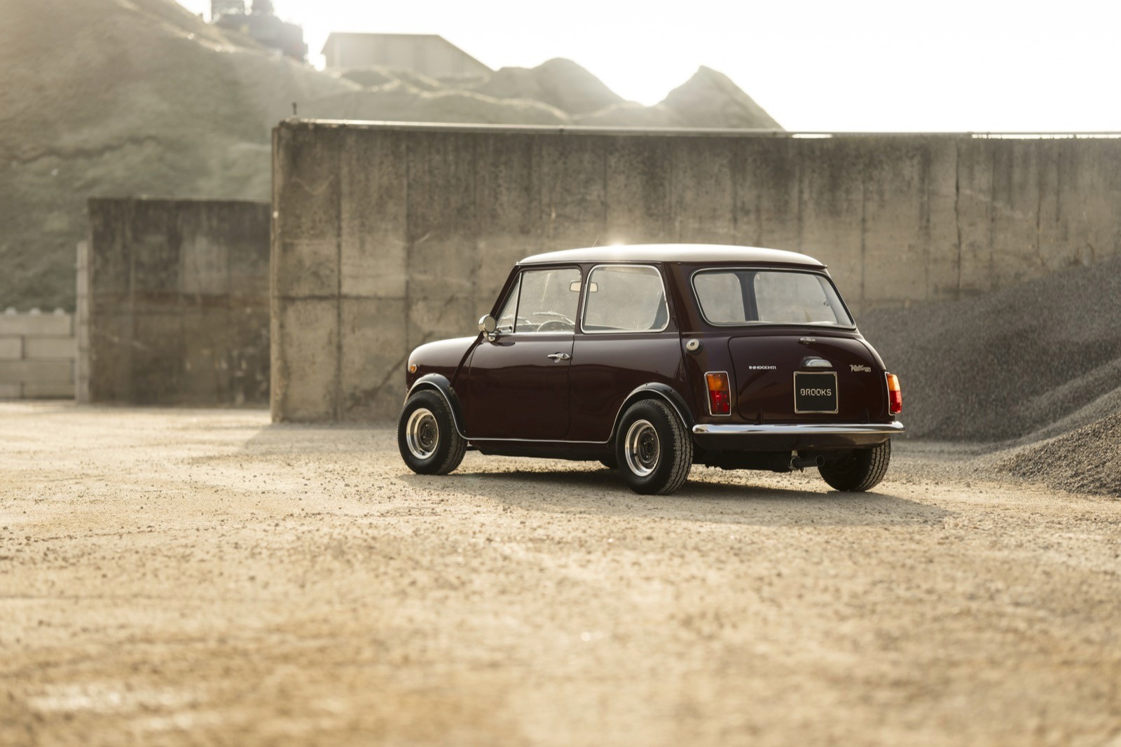 A vintage car parked on a sandy surface, with a concrete wall in the background and a hazy atmosphere.
