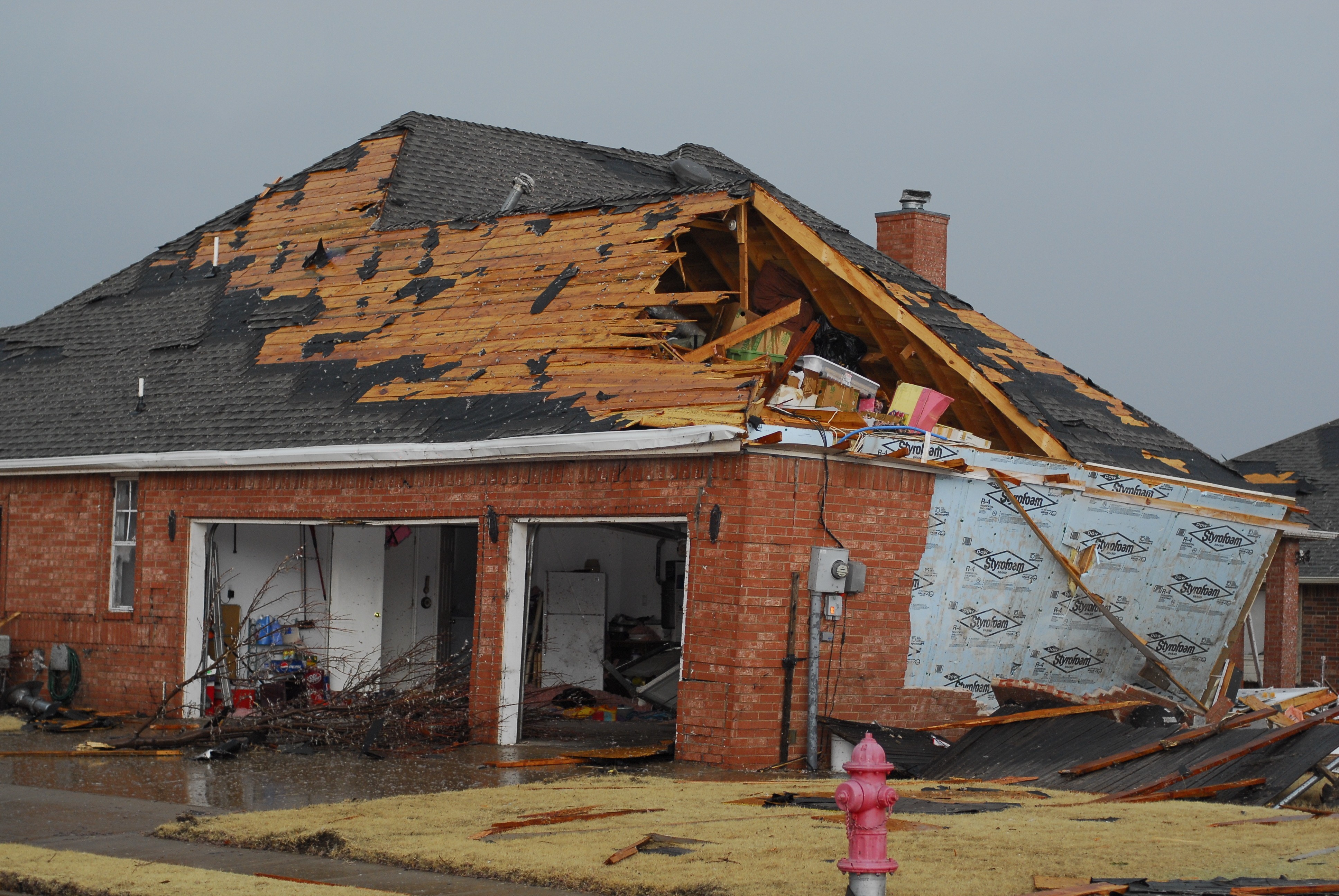 Severe storm damage to a residential roof in St. Louis with exposed rafters, torn shingles, and garage debris after wind and hail impact