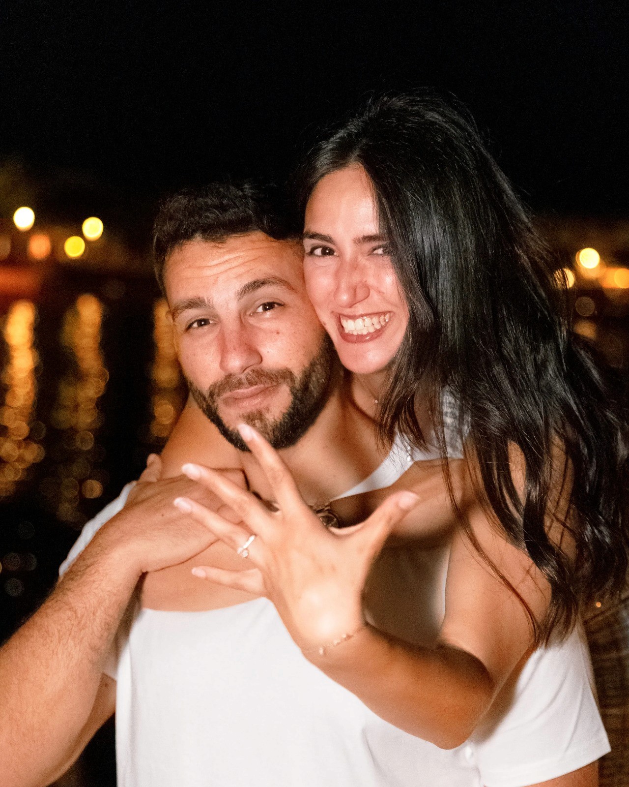 A close-up of two people holding hands, one wearing a denim jacket. The background is softly blurred, suggesting a tender, intimate moment in warm light.