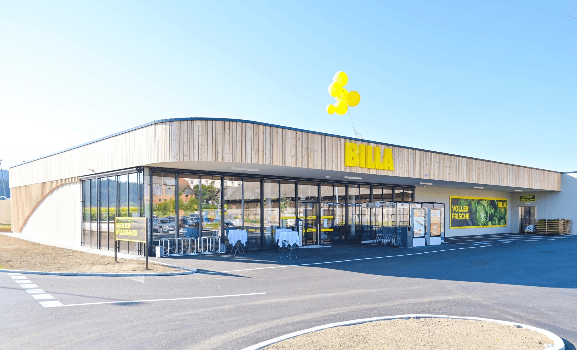 MW Interior  - Neueröffnung eines modernen Billa Supermarkts mit Holzfassade, Glasfront und gelben Luftballons" Beschreibung: Moderner Billa-Neubau mit natürlicher Holzverkleidung, großzügiger Glasfront und gelbem Markenauftritt – ein Referenzstandort, für den Ladeneinrichtung und Möblierung geliefert und realisiert wurden.