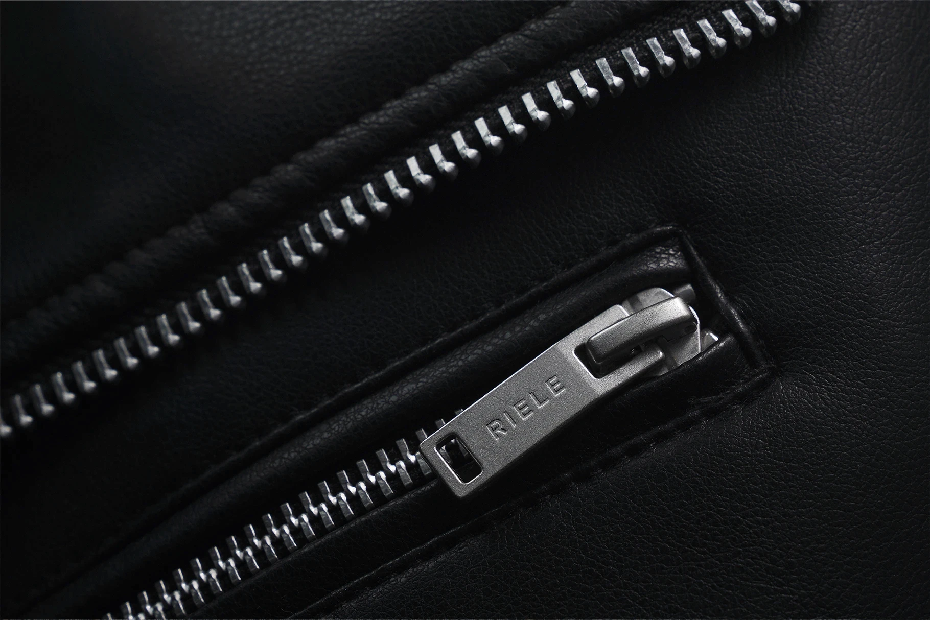 Close-up logo mockup on a silver zipper pull of a black leather jacket.