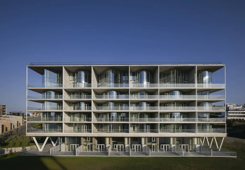  Full frontal view of a multi-level modern glass apartment complex built into a hillside.