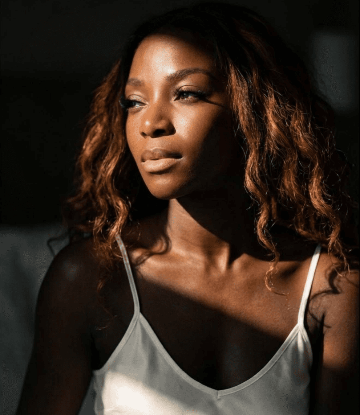 Close-up portrait of Freda in warm sunlight, gazing thoughtfully while wearing a white camisole.
