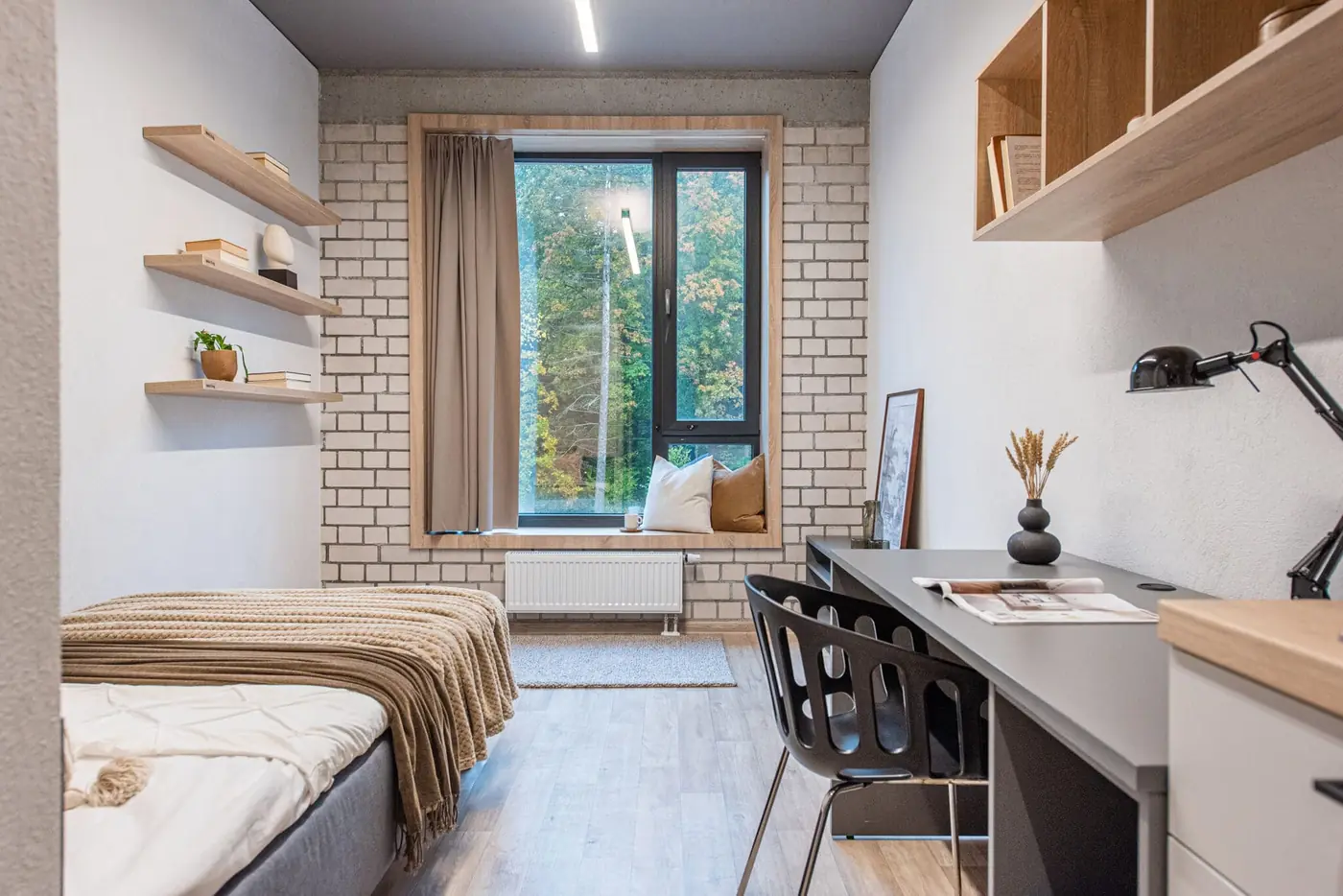 Single student studio in Vilnius with furnished sleeping area, study desk, shelving and large window.