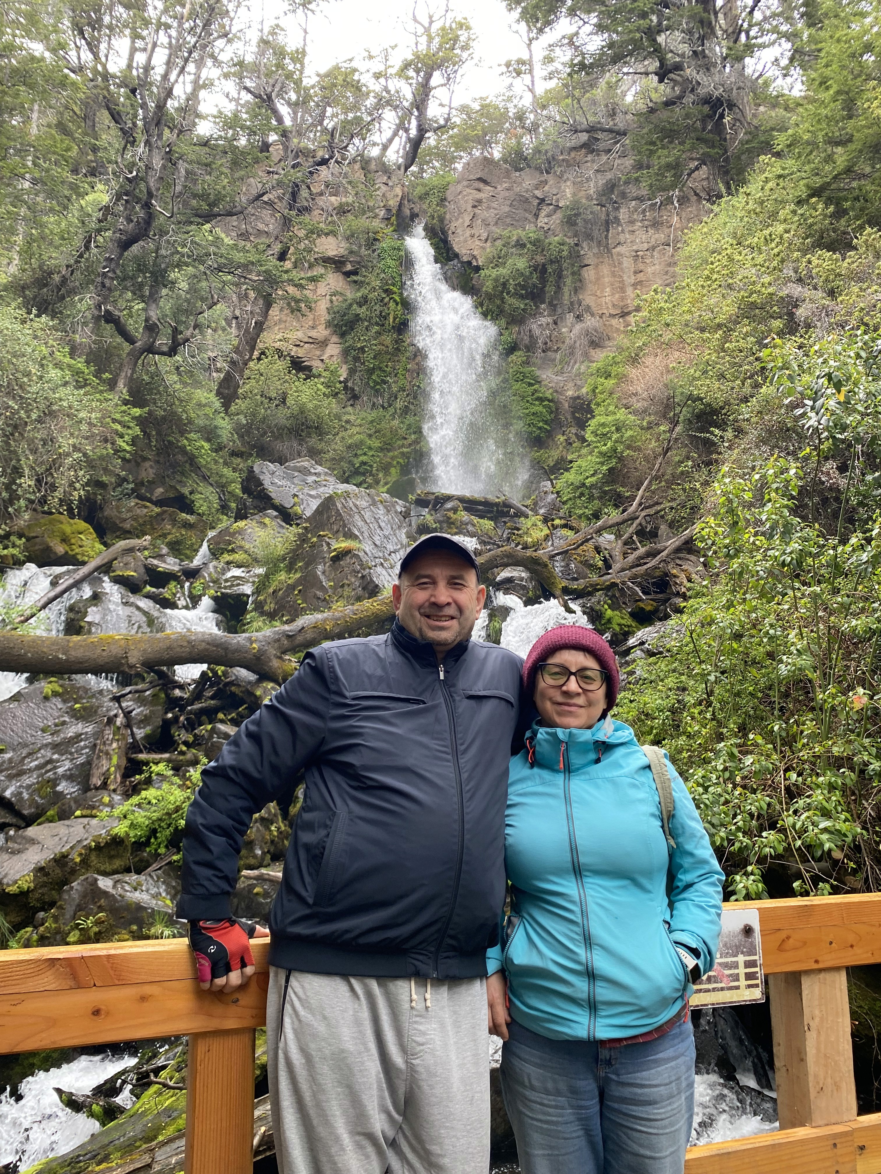 Mujer sentada sobre un tronco frente a una cascada doble en un bosque frondoso de Argentina.