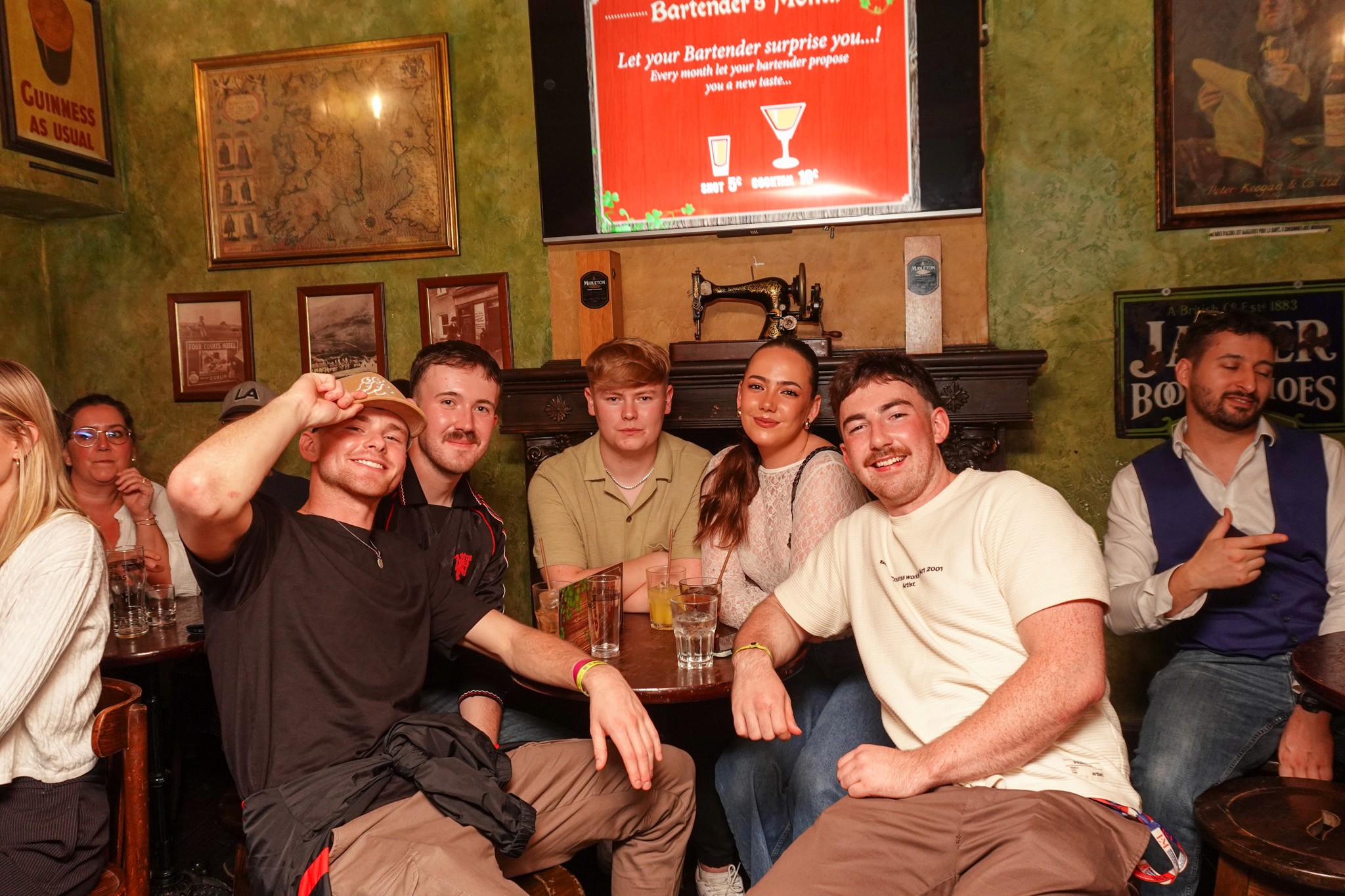 Group of young travelers sitting together around a table in a traditional pub during a bar crawl in Nice enjoying drinks smiling and socializing capturing the friendly group atmosphere and authentic nightlife experience of the French Riviera