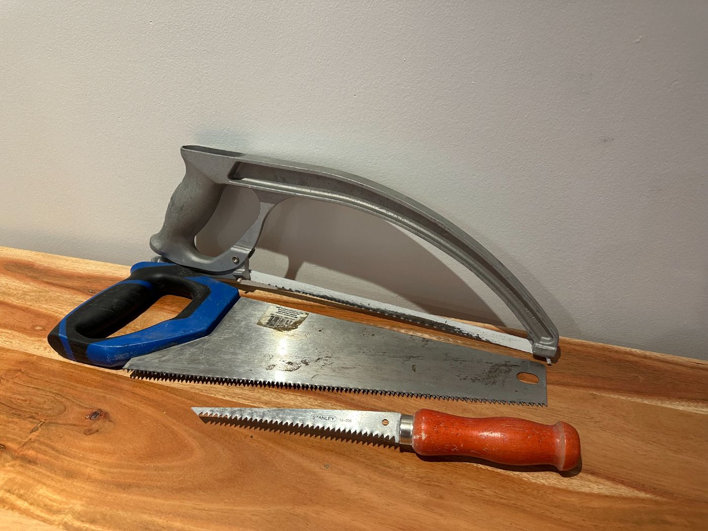 Ensemble de trois scies manuelles sur table en bois : scie à métaux, scie égoïne et scie à guichet Stanley avec manche en bois