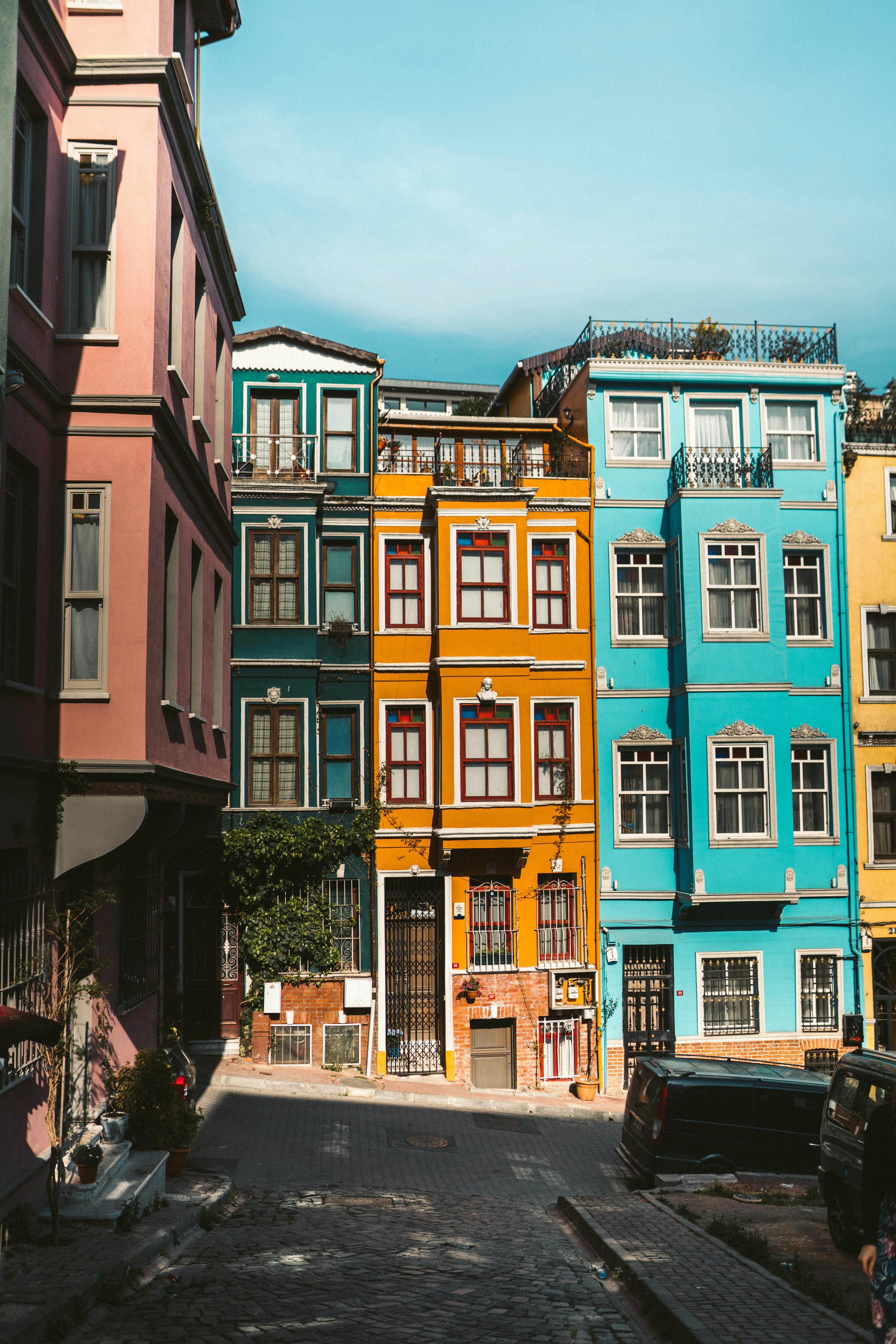 A steep cobblestone street lined with narrow, colorful row houses. The buildings are painted in vibrant shades of pink, teal, orange, and blue, featuring traditional wooden window frames.