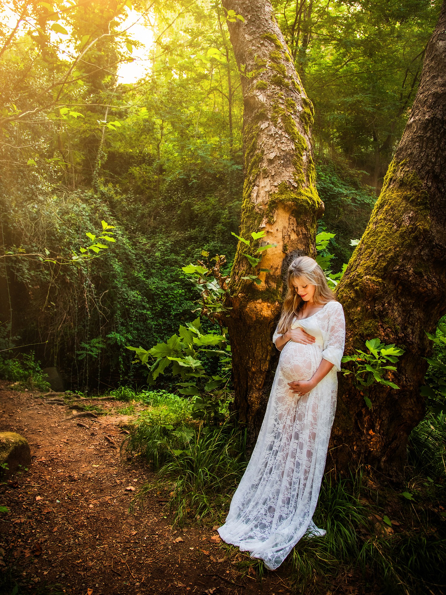 Premamá tocandose la barriga apoyada en un árbol