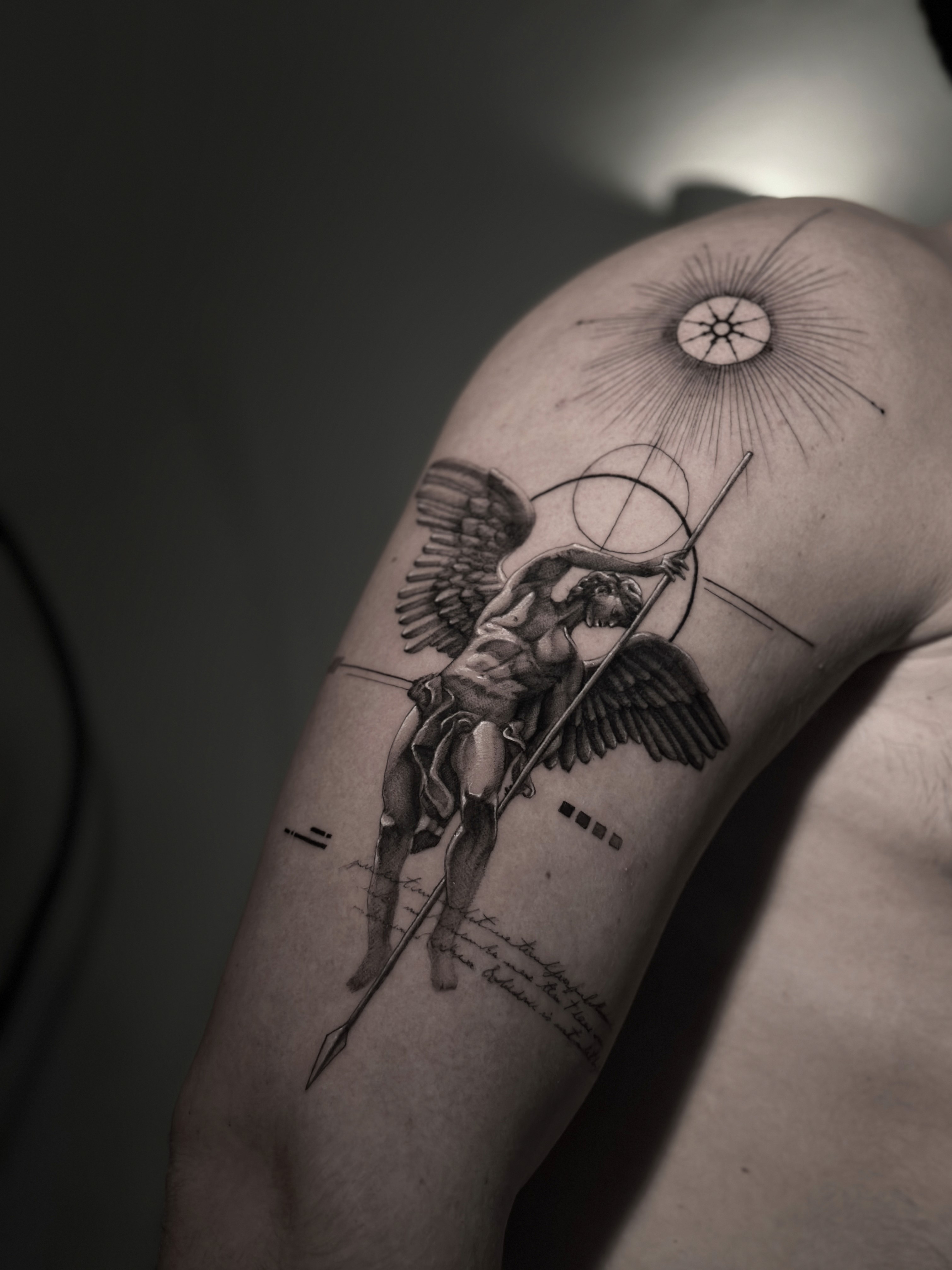Tattoo on a person’s arm depicting an angel returning a spear, with ancient inscriptions in the background, symmetrical geometry, and a sun on the shoulder.
