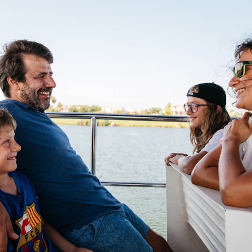 Cuatro personas sonríen y ríen durante un paseo en bote, con agua y vegetación de fondo.