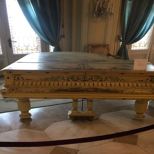 在一个优雅的房间里，有一架华丽的复古钢琴，配有青绿色窗帘和吊灯，钢琴盖上放着一个标牌。