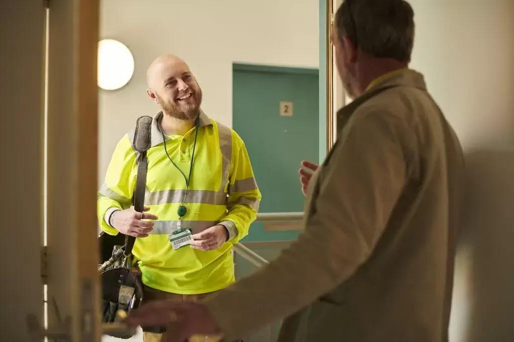 Man with high viability vest at a door, speaking to a gentleman and showing him a badge image