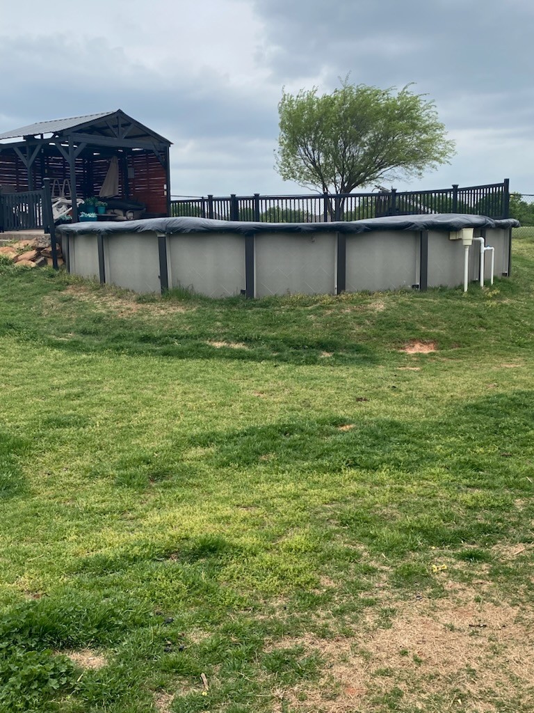 Exterior view of an above-ground, covered swimming pool in a residential yard with a lawn.