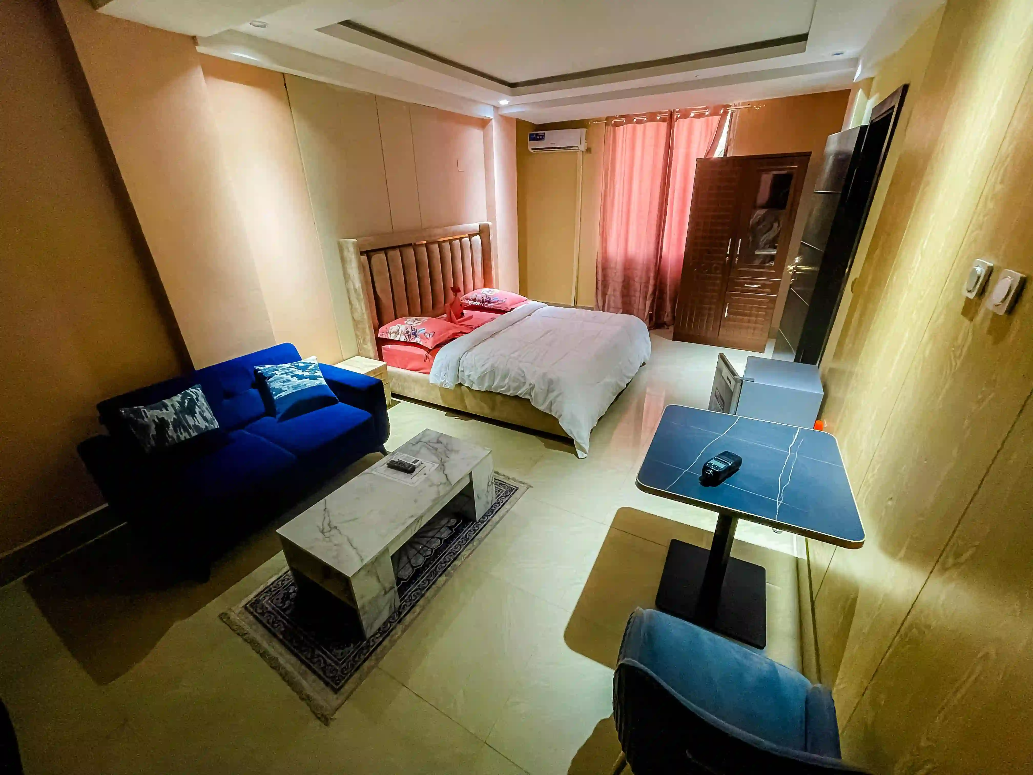 Chambre avec lit double, canapé bleu, table basse et fauteuil près de la fenêtre.