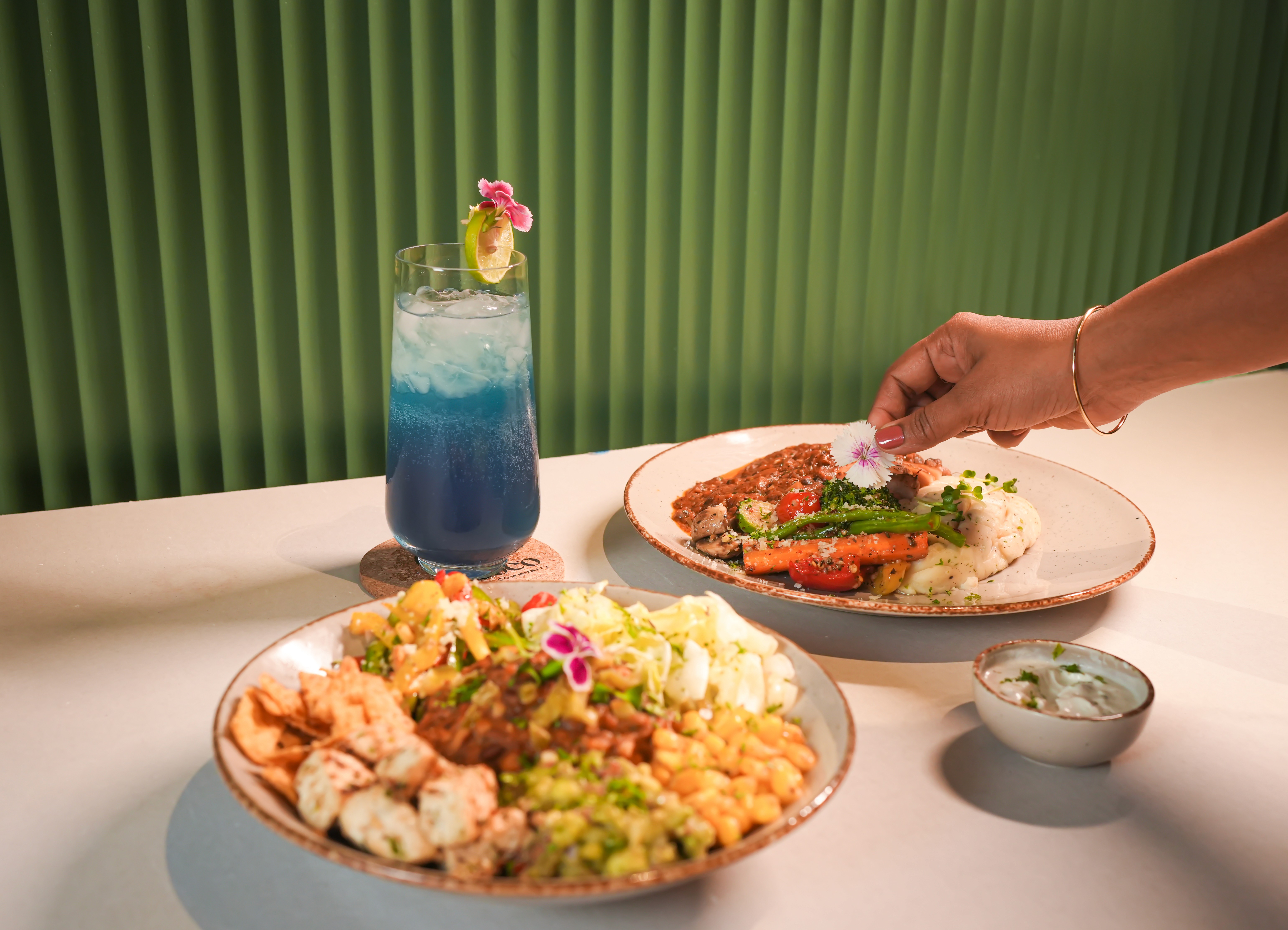 Two meals and a blue drink on a white table.