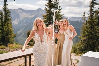 The bride and bridesmaids laugh as a champagne bottle sprays on the cabin deck.