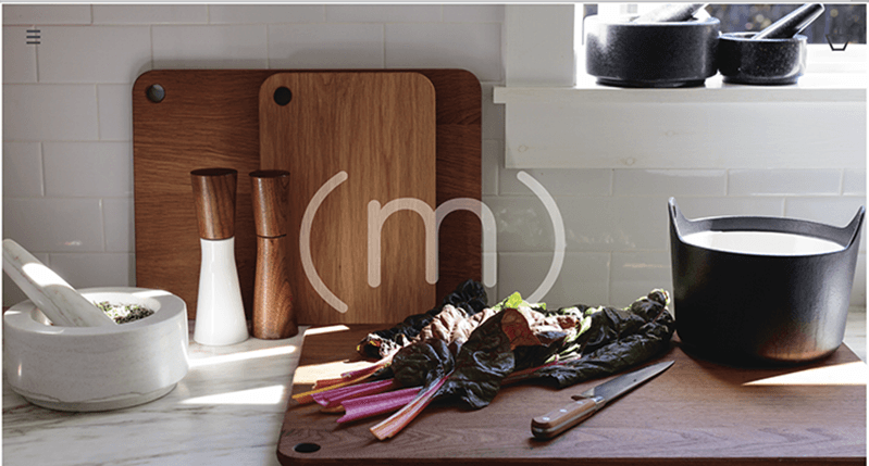 A photo of a kitchen's table, filled with different tool and some vegetables on which a few rays of sunlight shine trough a window.