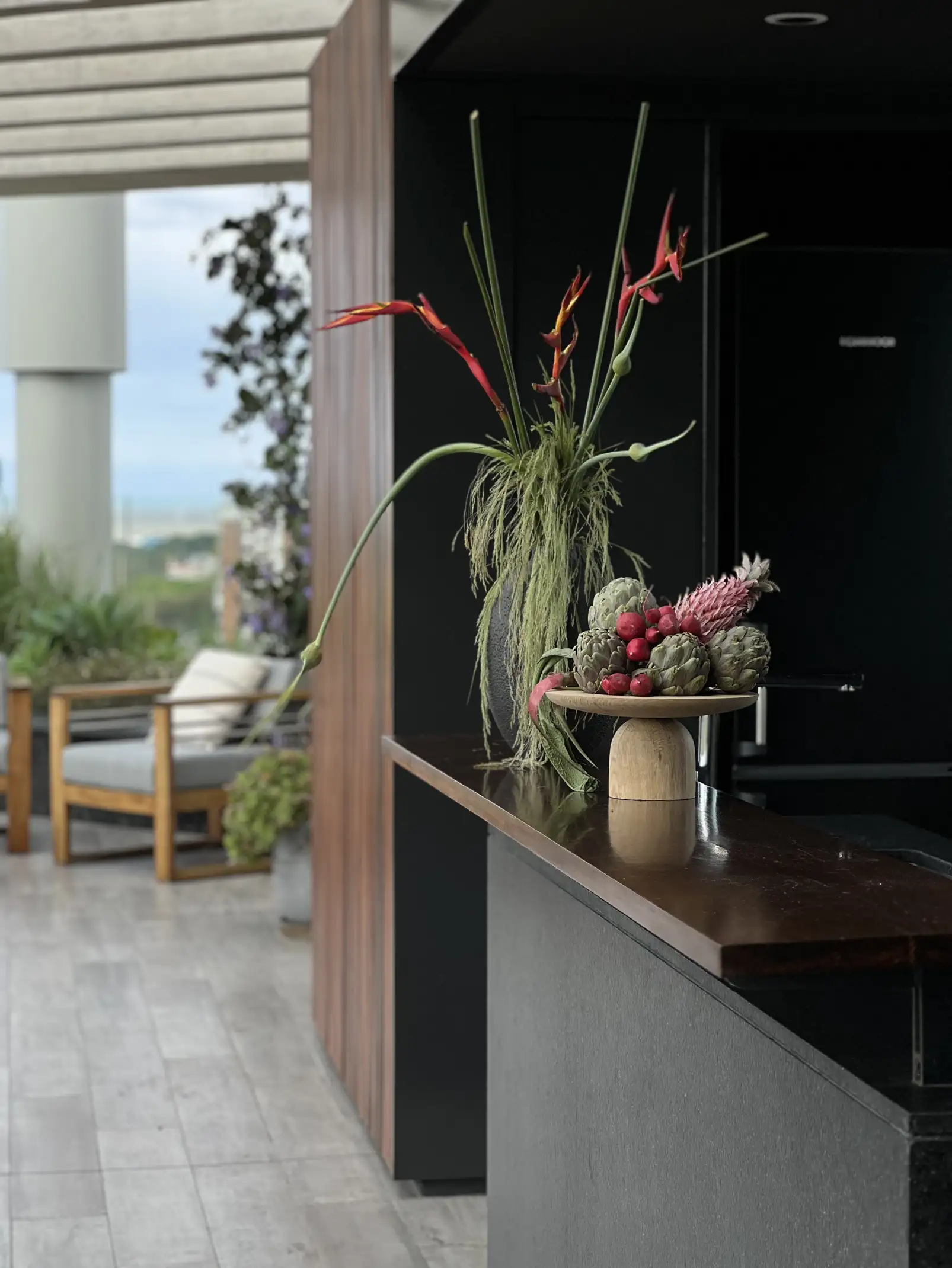 Instalación floral con heliconias y frutas sobre barra exterior para proyectos de paisajismo que integran color y textura en terrazas modernas.