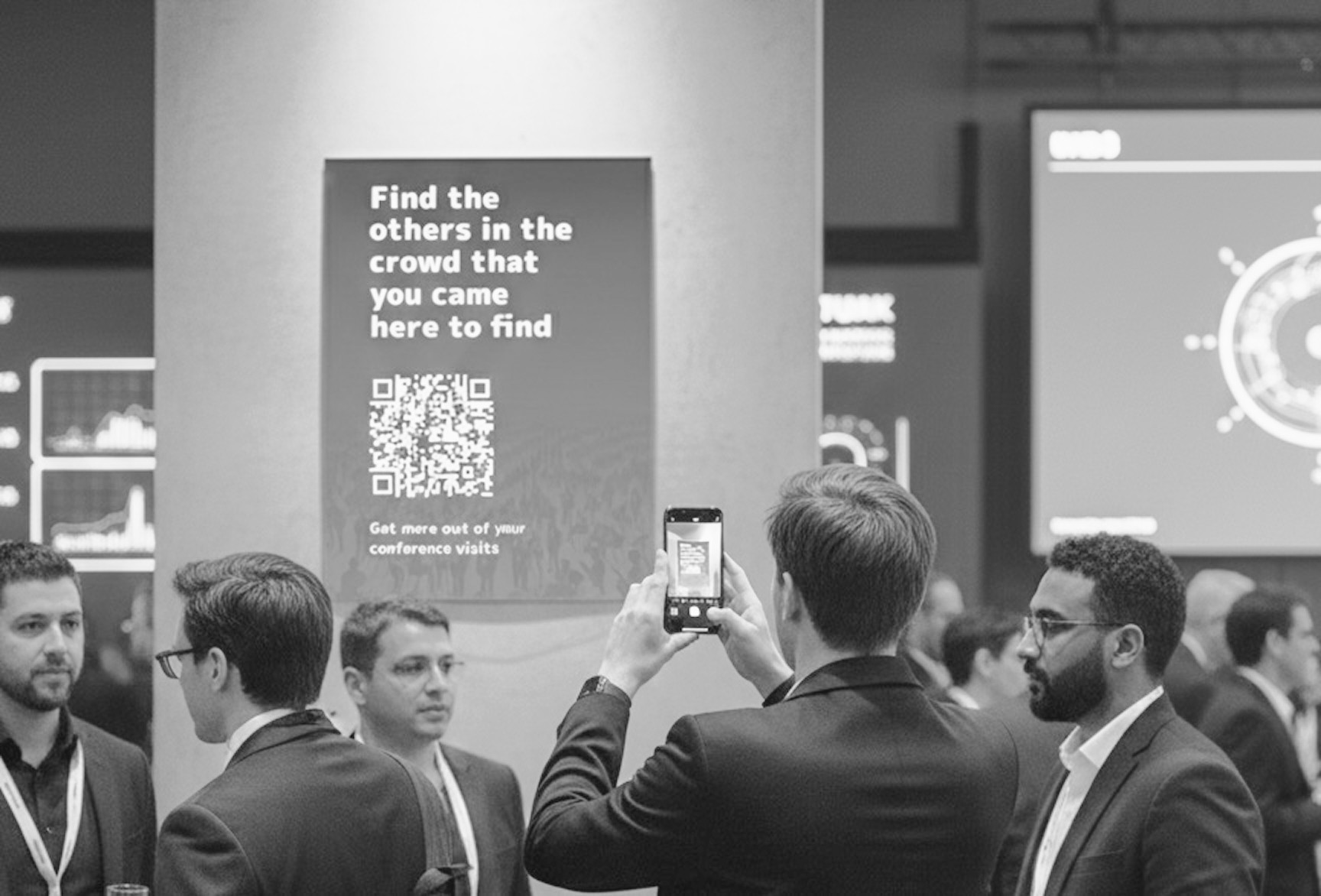 View of a conference hall with a poster on the wall, stating "Find the others in the crowd that you came here to find", above a QR code.