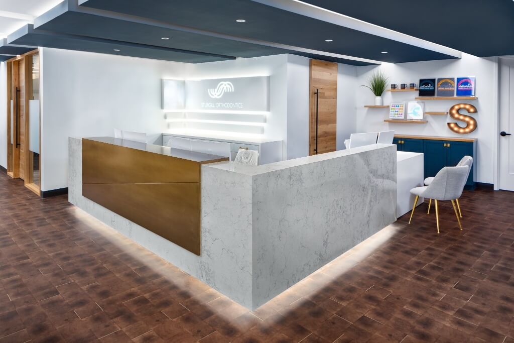 Modern reception area with a wooden front desk and minimalist design, featuring white walls and wooden flooring.