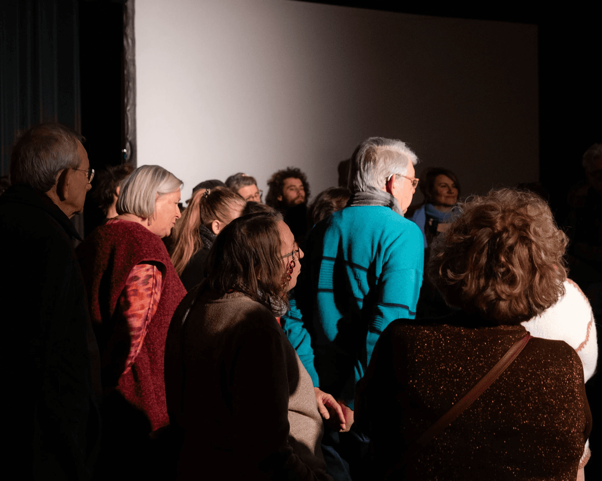De foto toont de ruggen van een groep mensen die rechtstaand naar de presentatie luisteren.