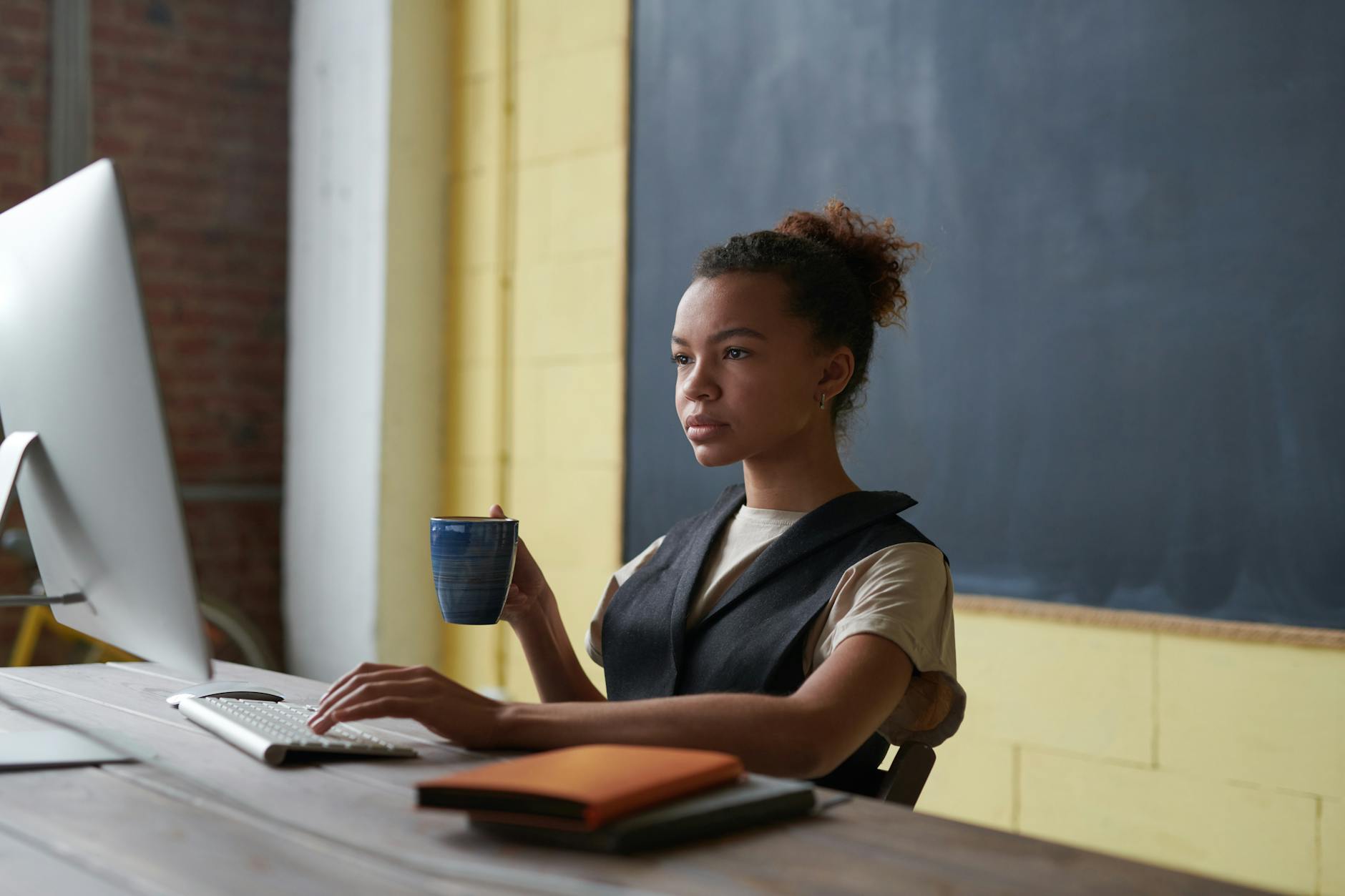 A teacher drinking coffee while browsing online courses for teachers on a laptop at a kitchen table.