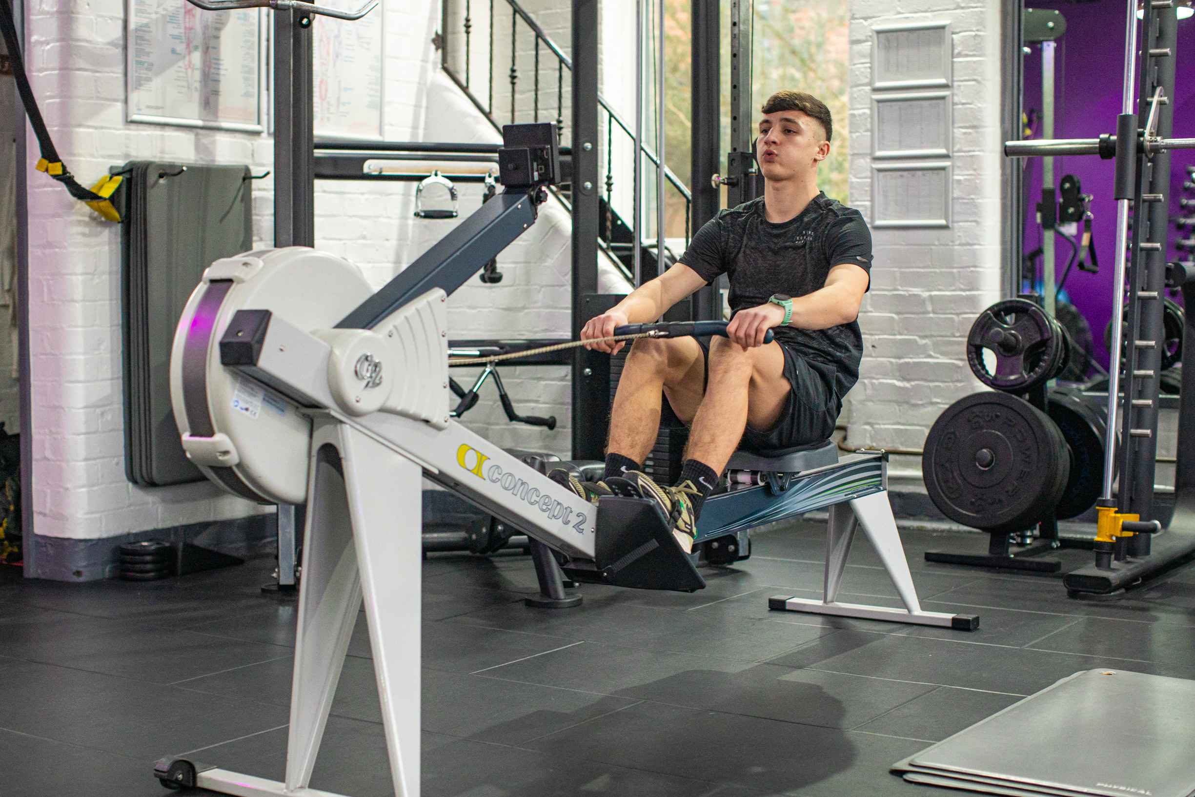 An Alchemy fitness enthusiast utilizes a rowing machine in a gym setting as part of his New Year's resolution