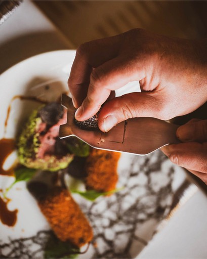 Chef Norman Van Aken in white uniform carefully plating food in professional kitchen