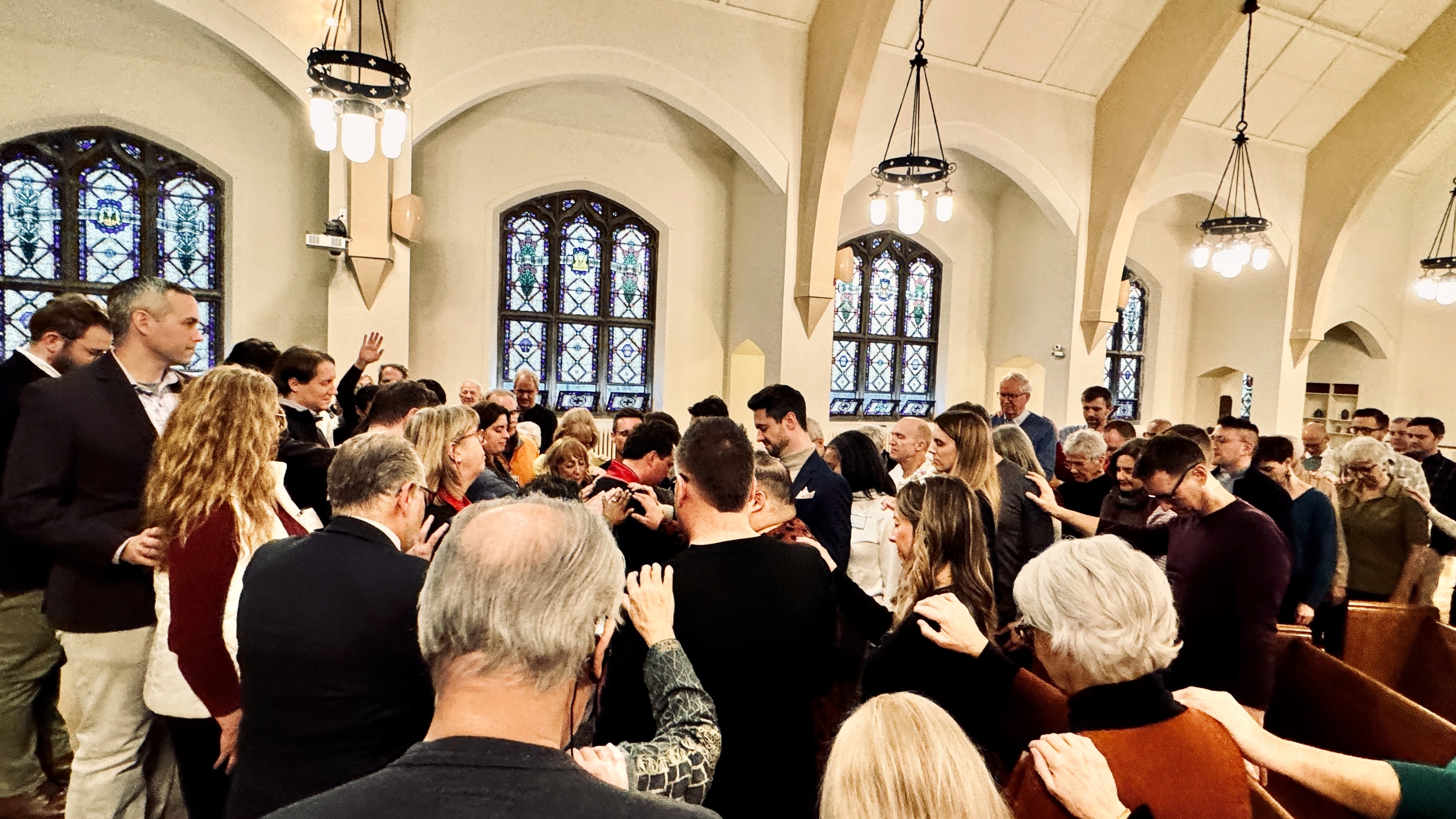 A large group of Grace Trinity Church members gathered closely in prayer, laying hands on one another in the sanctuary.