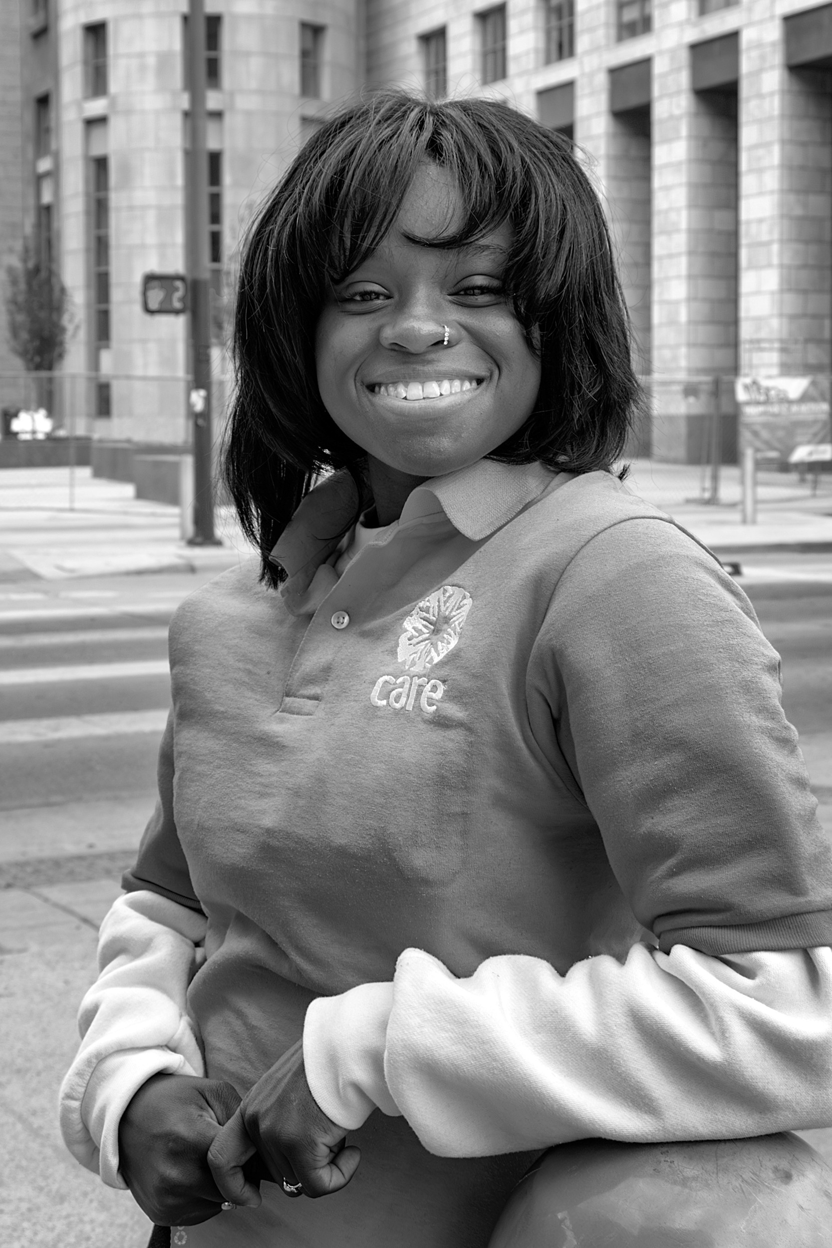Portrait of a smiling woman wearing a CARE organization sweatshirt standing at a crosswalk
