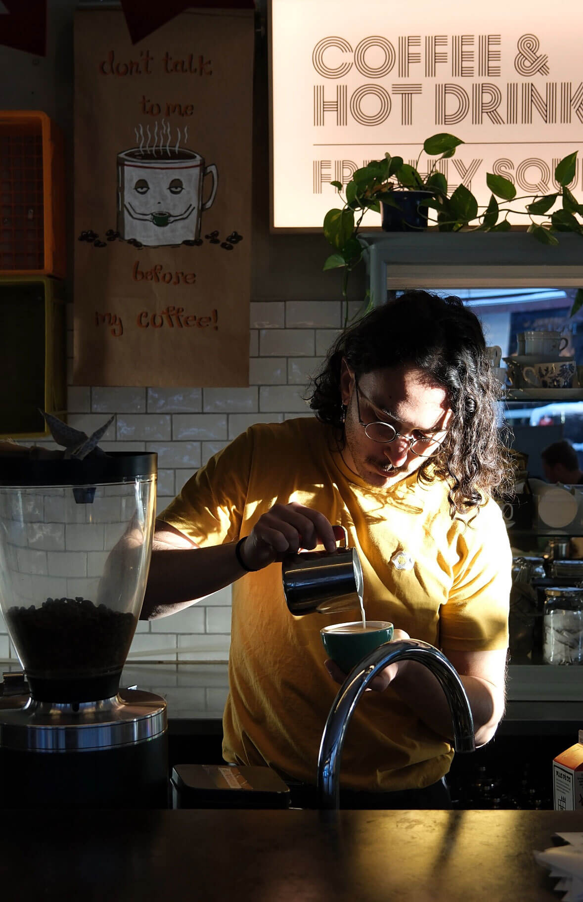 Barista standing behind the bar and making a latte coffee.